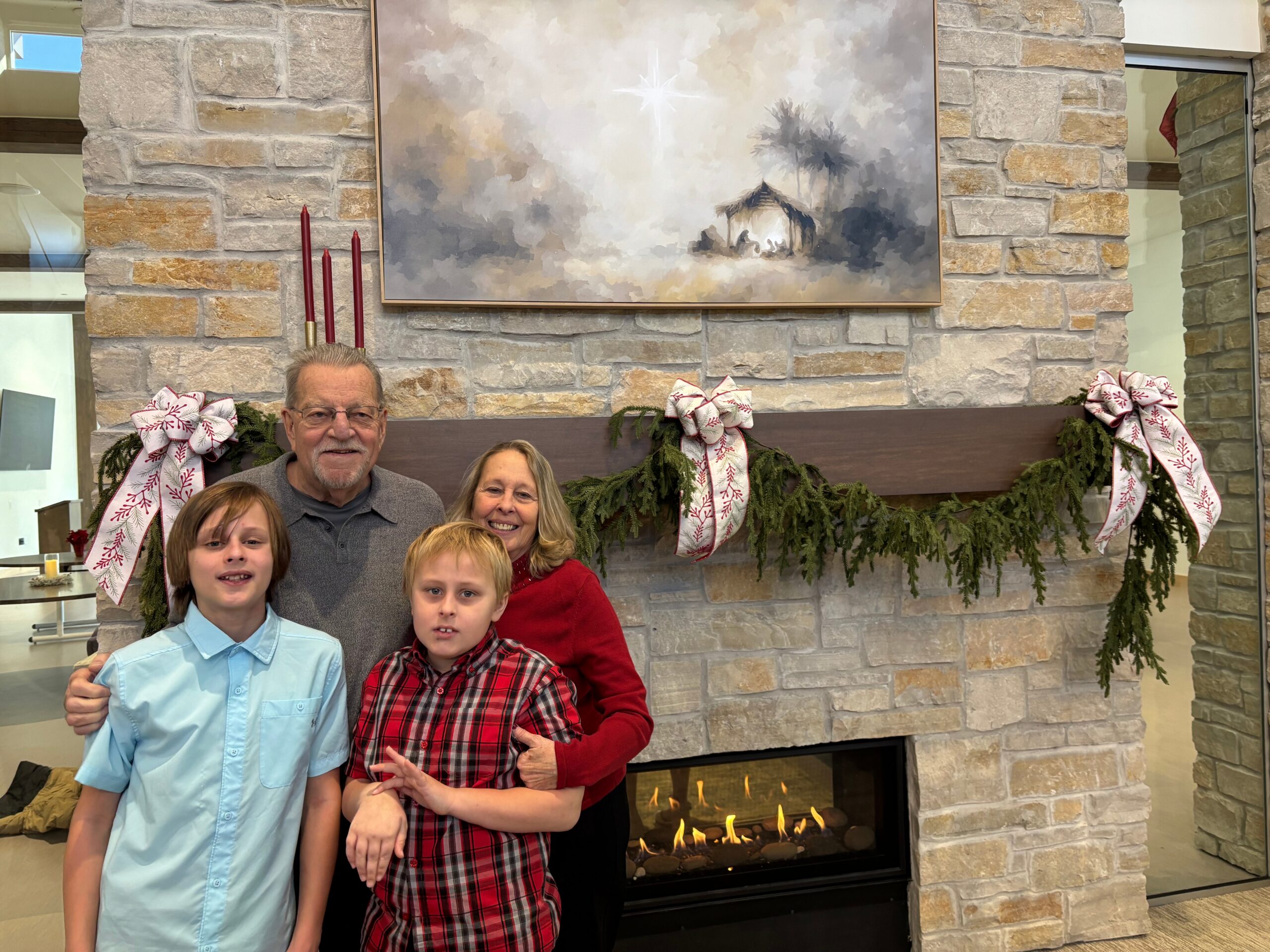 Family of five posing together in front of a stone fireplace with holiday garlands and a large painting above the mantle.