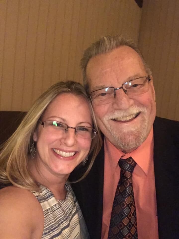 Smiling woman and man pose for a close-up selfie indoors; both wear glasses and lean in together.