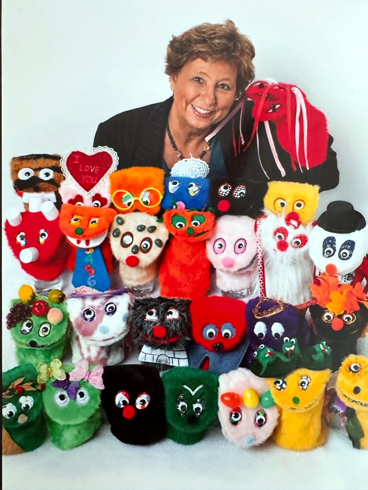 Smiling woman posing with a colorful display of handmade sock puppets arranged in front of her.