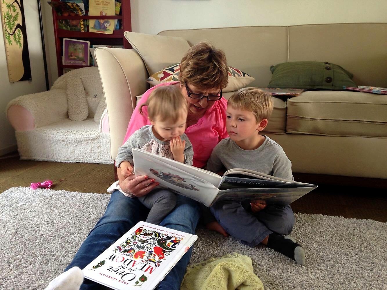 Woman reading with two young children on a living room rug.