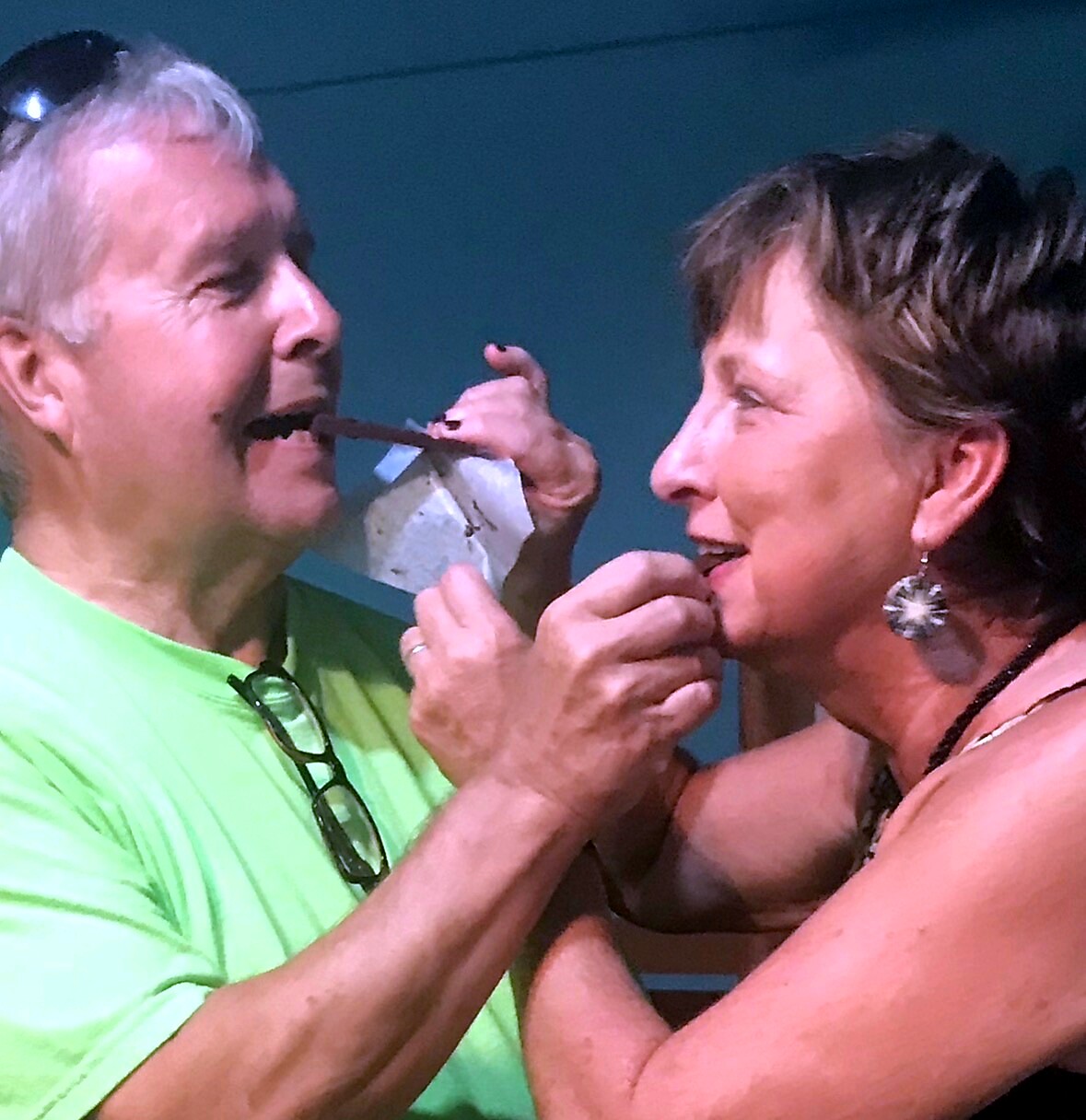 Playful moment as a man feeds a chocolate treat to a smiling woman.