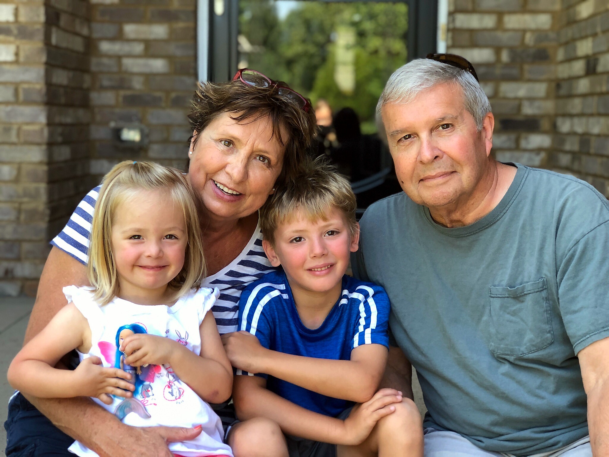 Family of four posing for a photo outside a brick building: mother, father, and two smiling children close together.