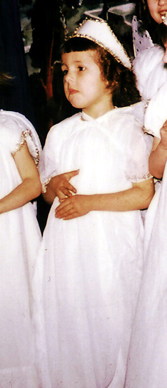 Young girl in a white dress with a silver crown, standing with others in a group event.