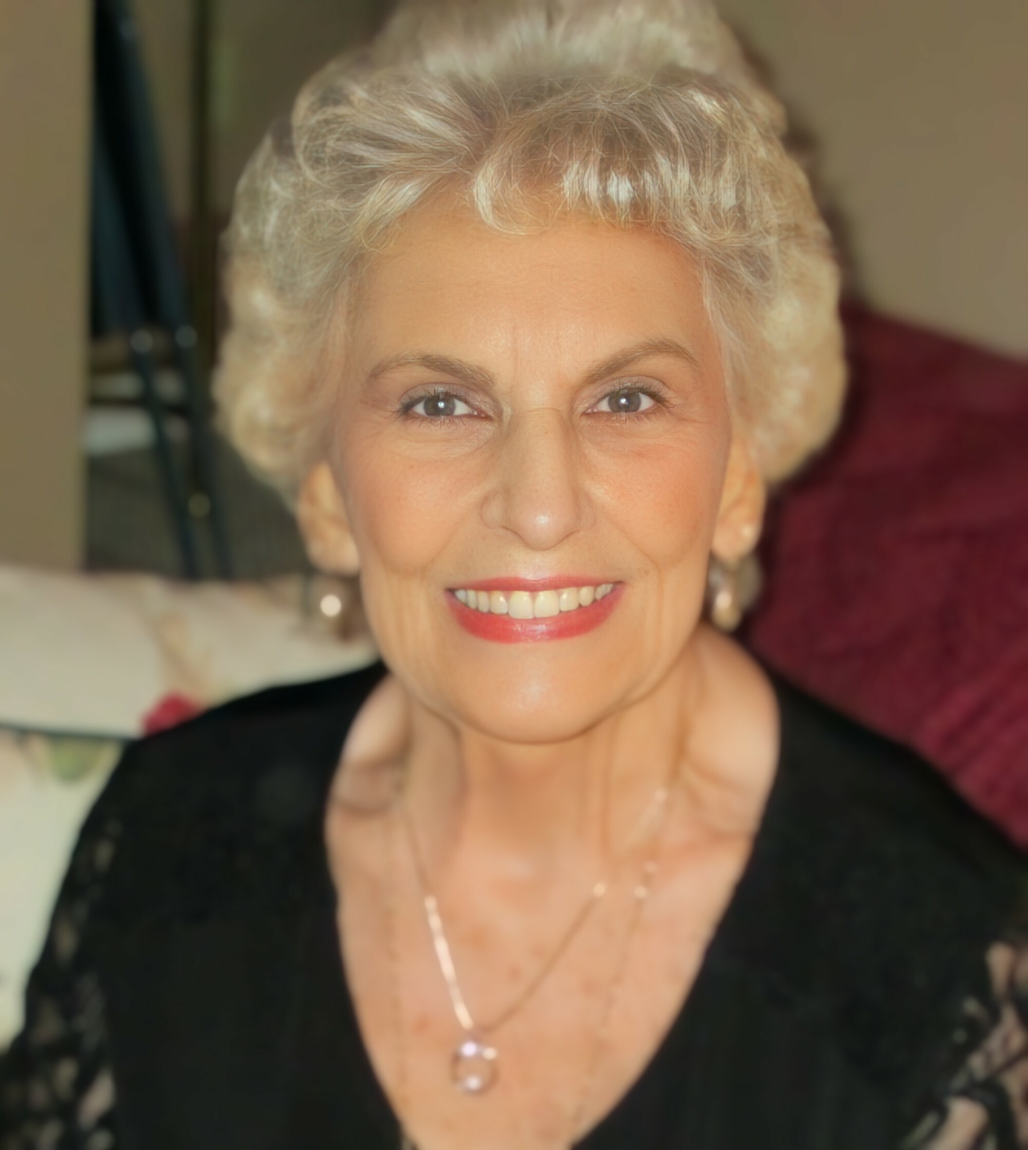 Smiling elderly woman with short gray hair, wearing a black top and a pendant necklace.