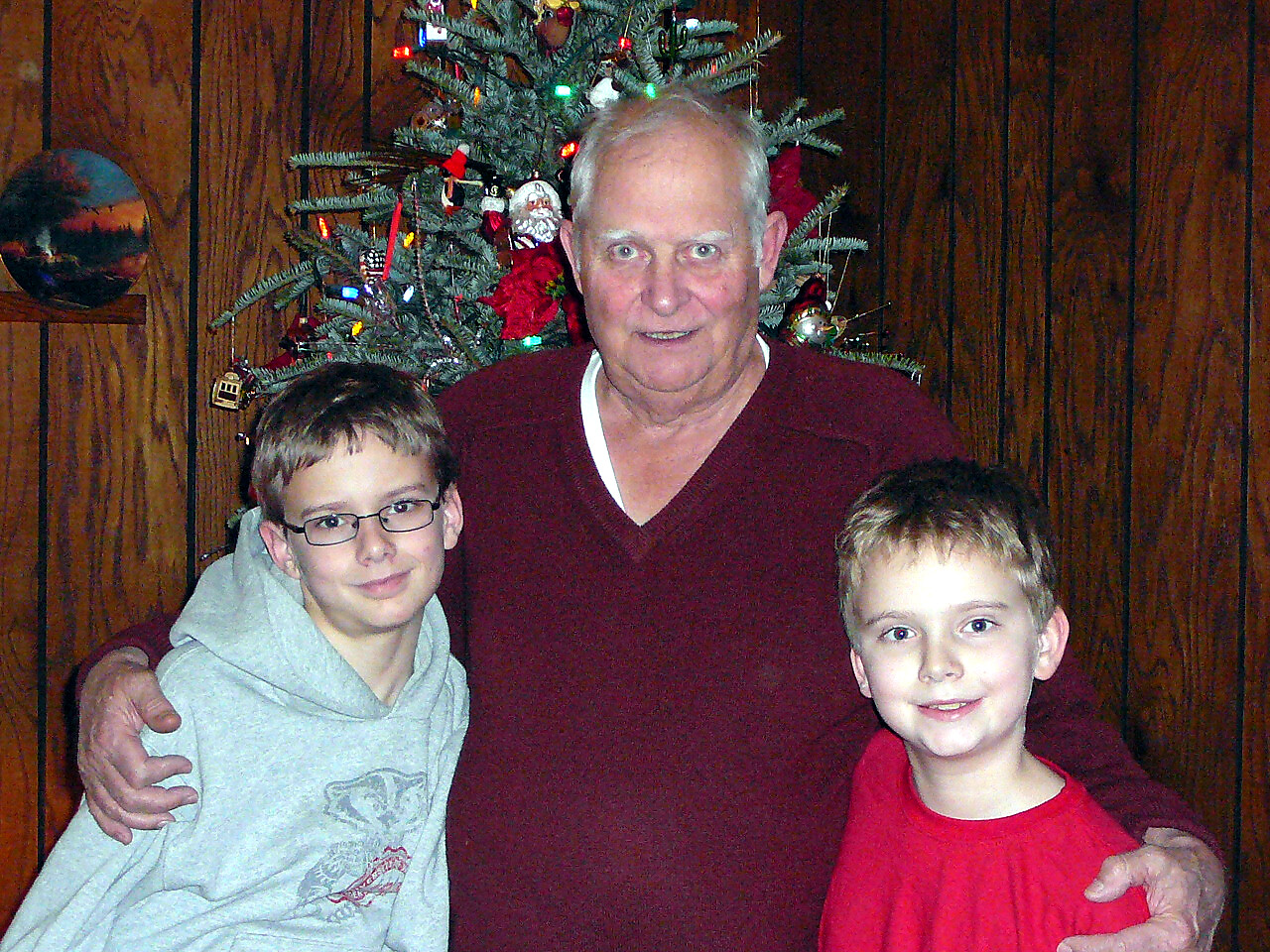 Grandfather posing with two boys in front of a decorated Christmas tree indoors.