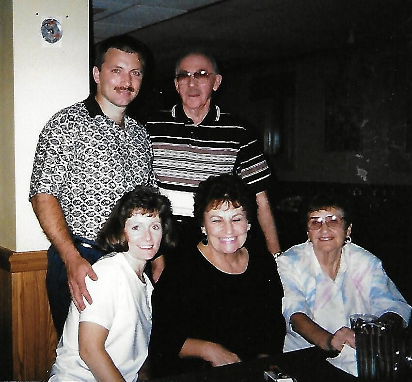 Group of five adults posing together indoors, some seated and others standing behind them, smiling at the camera.