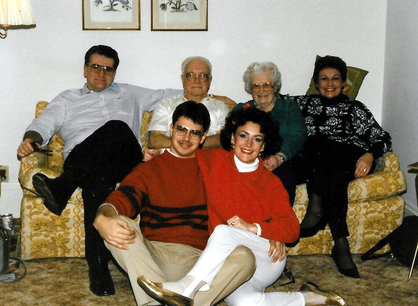 Six family members posing for a photo on a yellow patterned sofa in a living room, smiling at the camera.