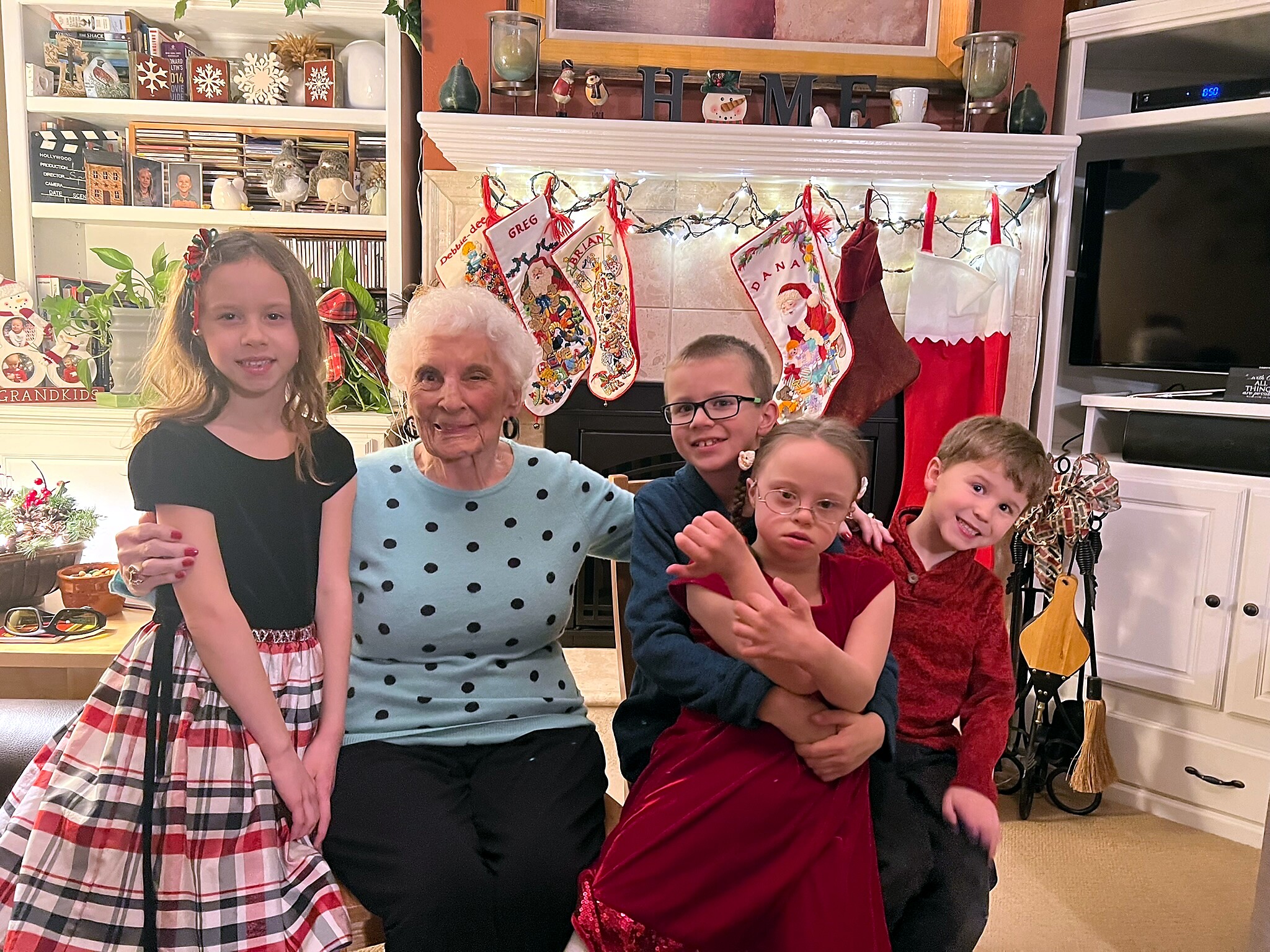Family posing for a Christmas photo in a festively decorated living room with stockings hanging over the fireplace and holiday decorations behind them.