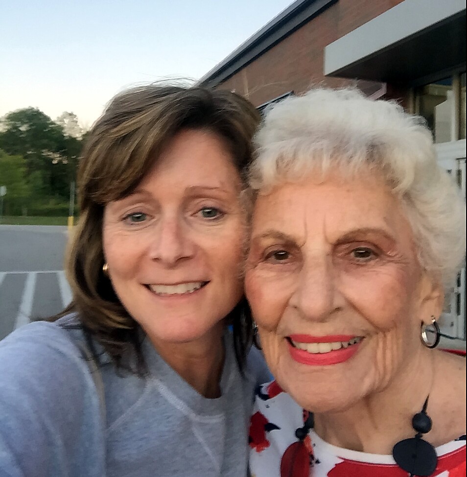 Two smiling women taking a selfie outdoors beside a brick building, posing closely together.