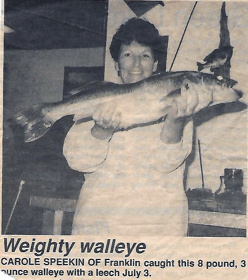 Smiling woman holding a large walleye in a room, headline reads 'Weighty walleye' (news photo).
