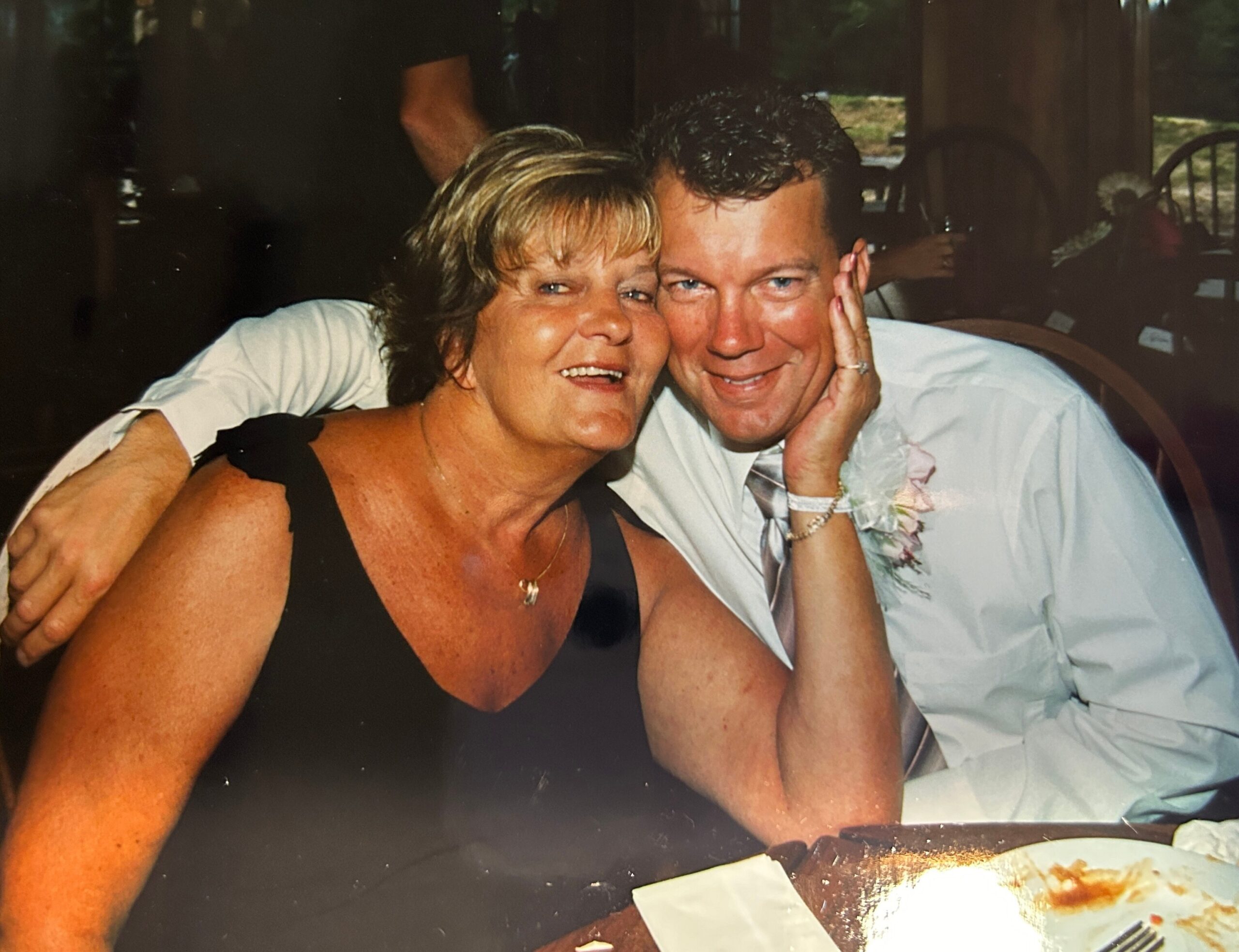 A smiling couple embraces for a photo at a celebration, with their heads close together and the woman in a black dress.
