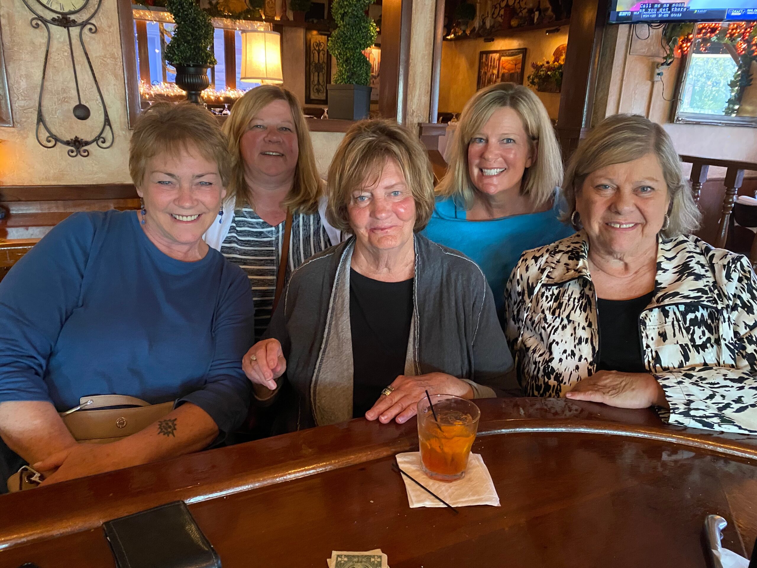 Five women seated at a restaurant table, smiling for a group photo with drinks and napkins in front of them.
