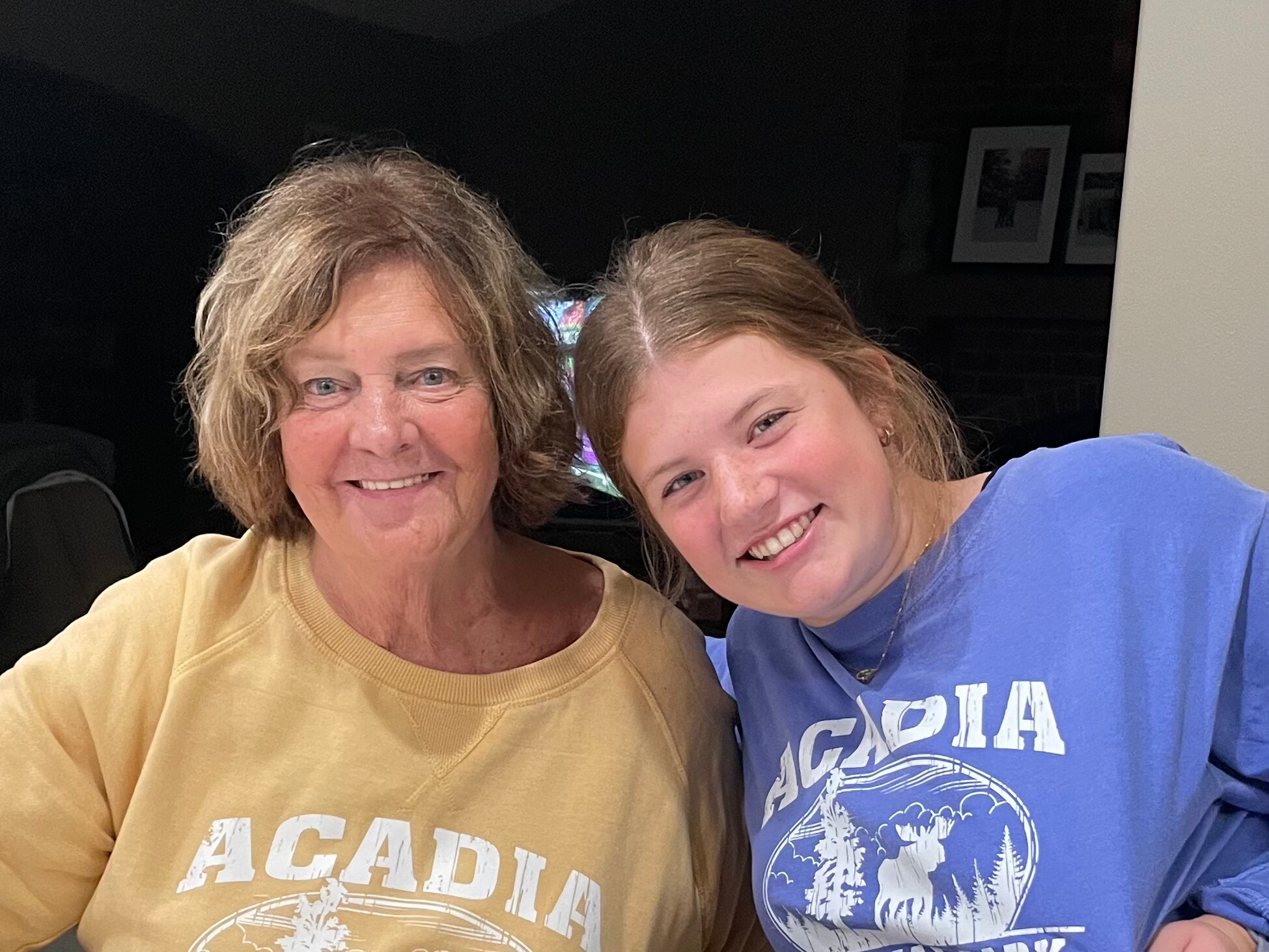 Two women smiling for a selfie, wearing tan and blue sweatshirts with a graphic design on the front.