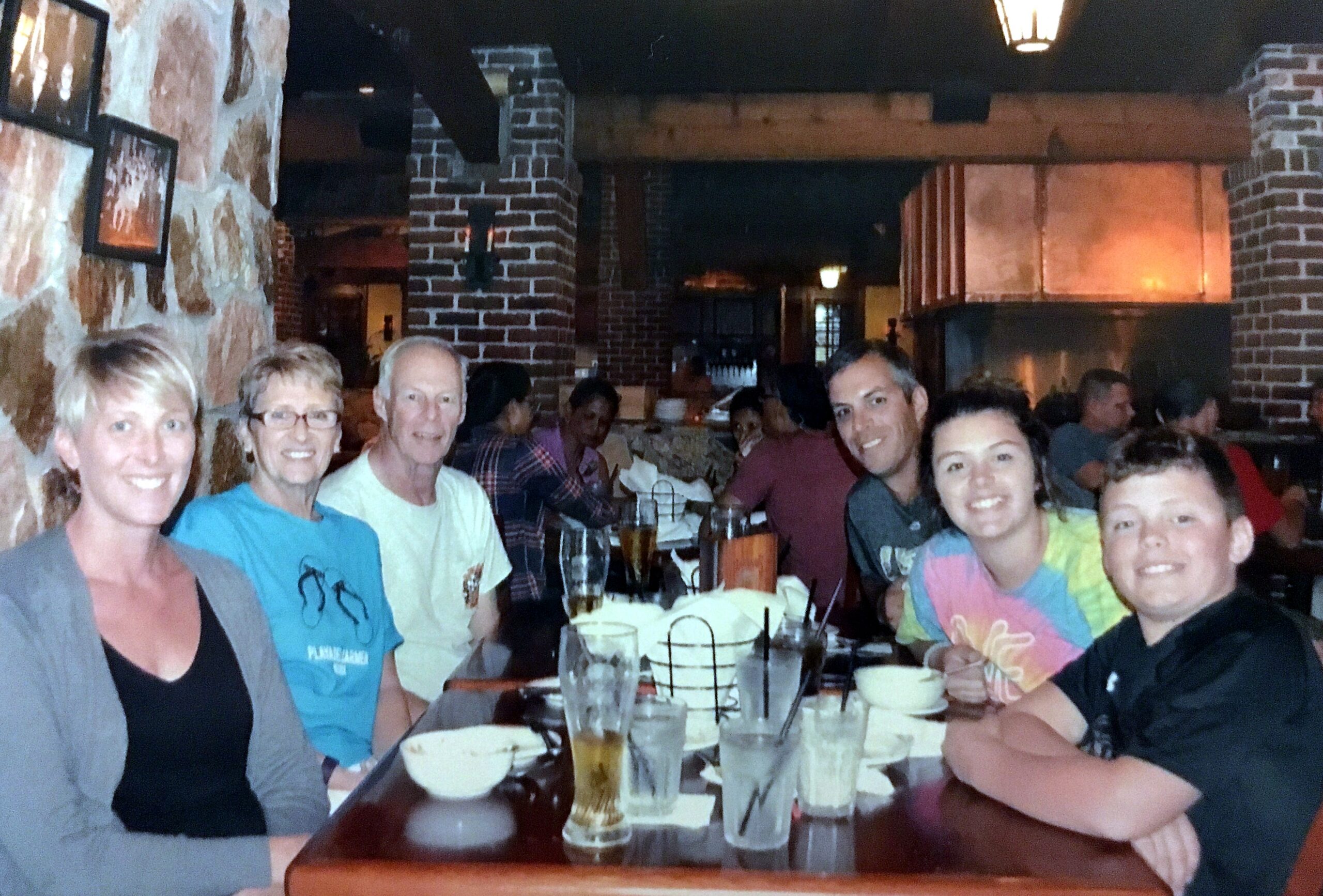 Group of smiling people seated around a restaurant table with drinks and bowls, posing for a photo.