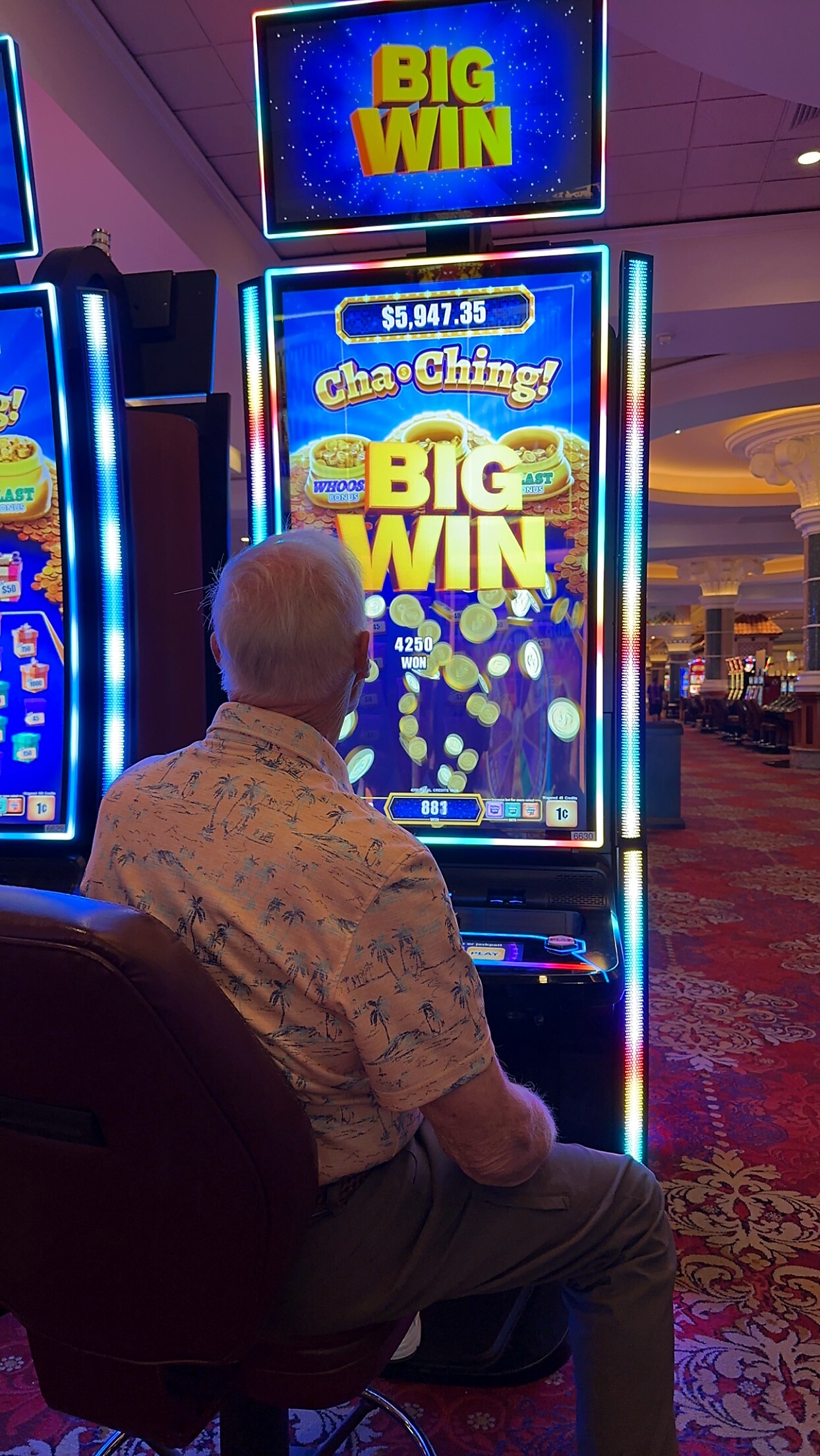Older man in a tropical shirt sits at a brightly lit slot machine, screen shows 'BIG WIN' with coins exploding on the display.