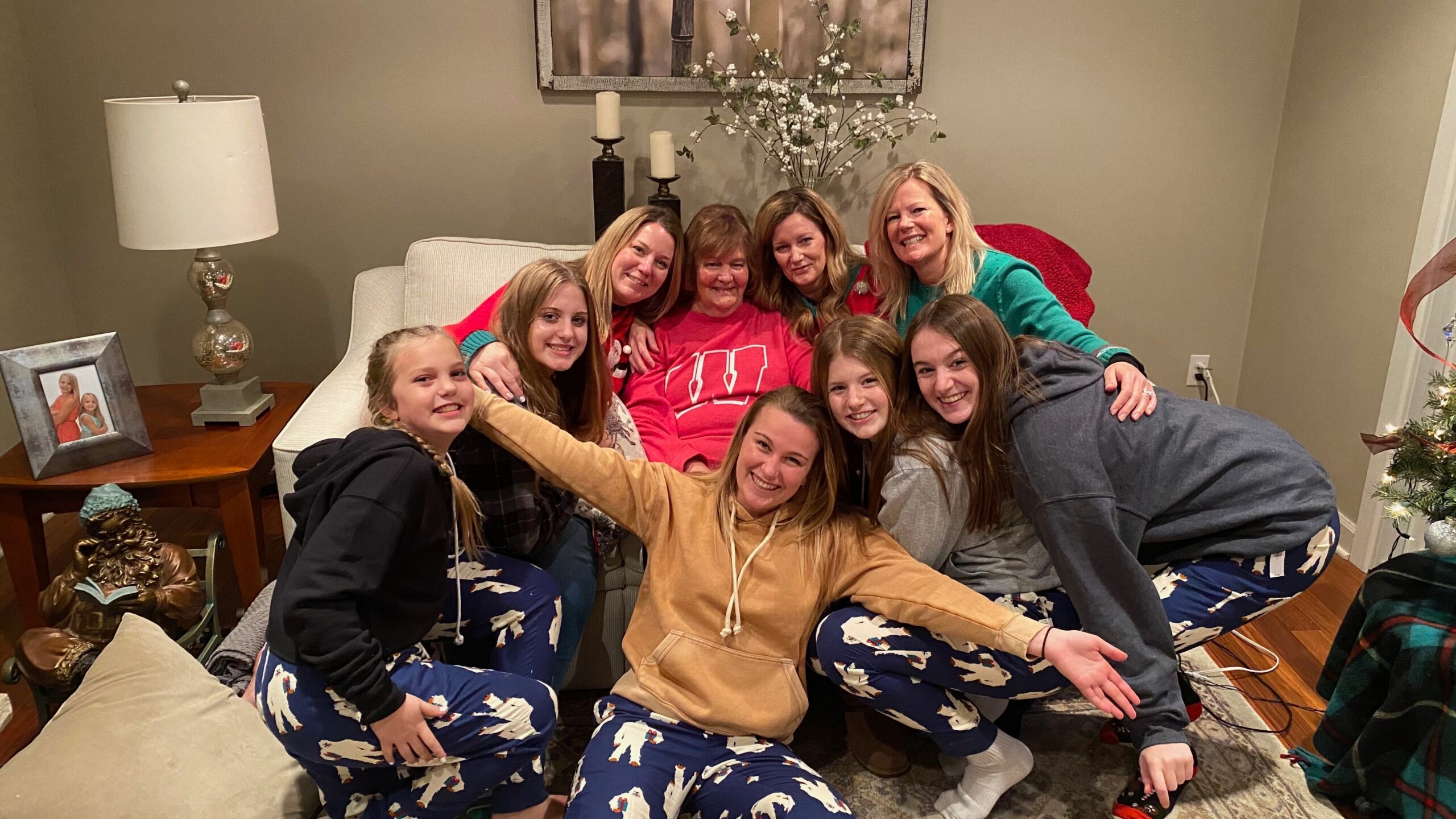 Group of women and girls posing for a photo on a sofa in a cozy living room, smiling and hugging.