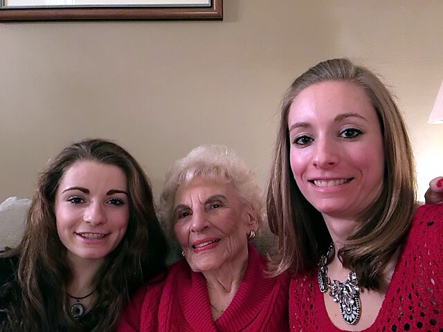 Three generations of women smiling while sitting on a couch together in a living room.