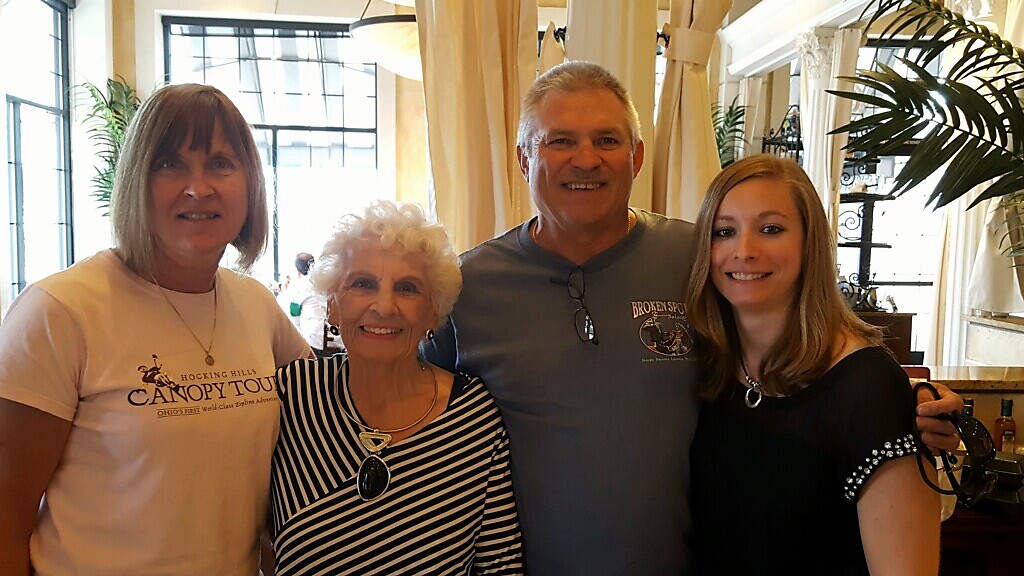Four adults posing for a photo in a sunlit indoor space with plants and draped curtains.