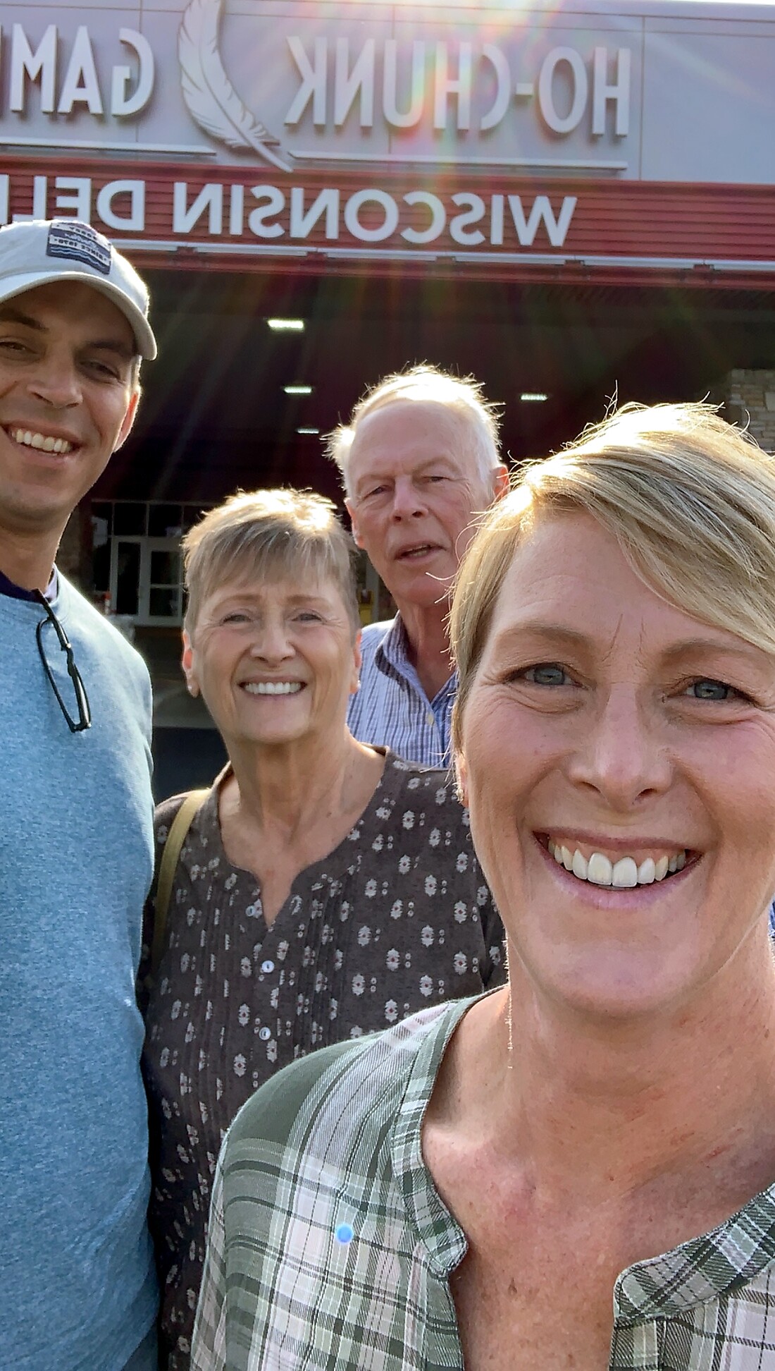 Four adults smiling for a selfie in front of a storefront with red signage and sun glare in the photo.