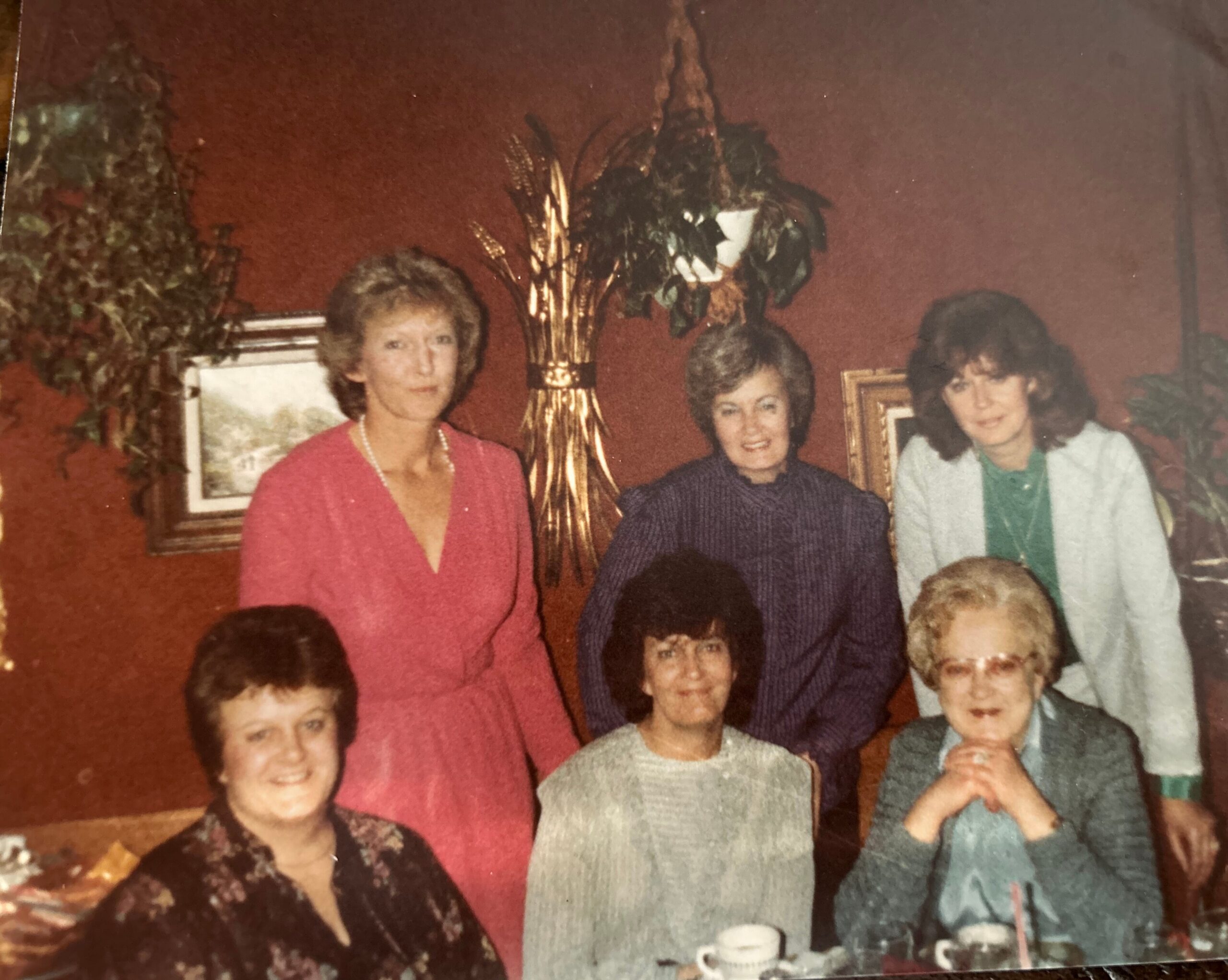 Group of people posing for a family photo at a dinner table in a room with a red wall and tall plant in the background.