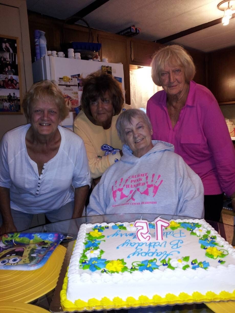 Four women celebrate a 21st birthday around a decorated cake on a kitchen counter, smiling at the camera.