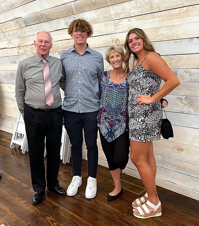 Four family members pose together indoors against a light wood wall, smiling at the camera.