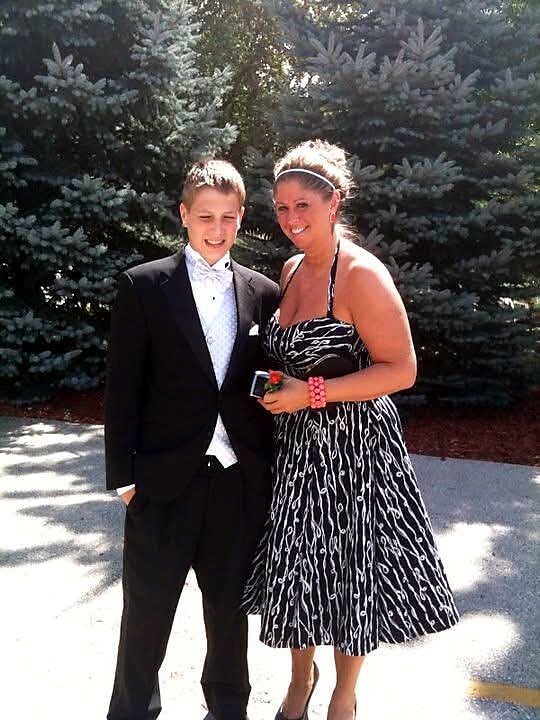 Young man in a black tuxedo posing with a woman in a black-and-white patterned dress outdoors, both smiling.