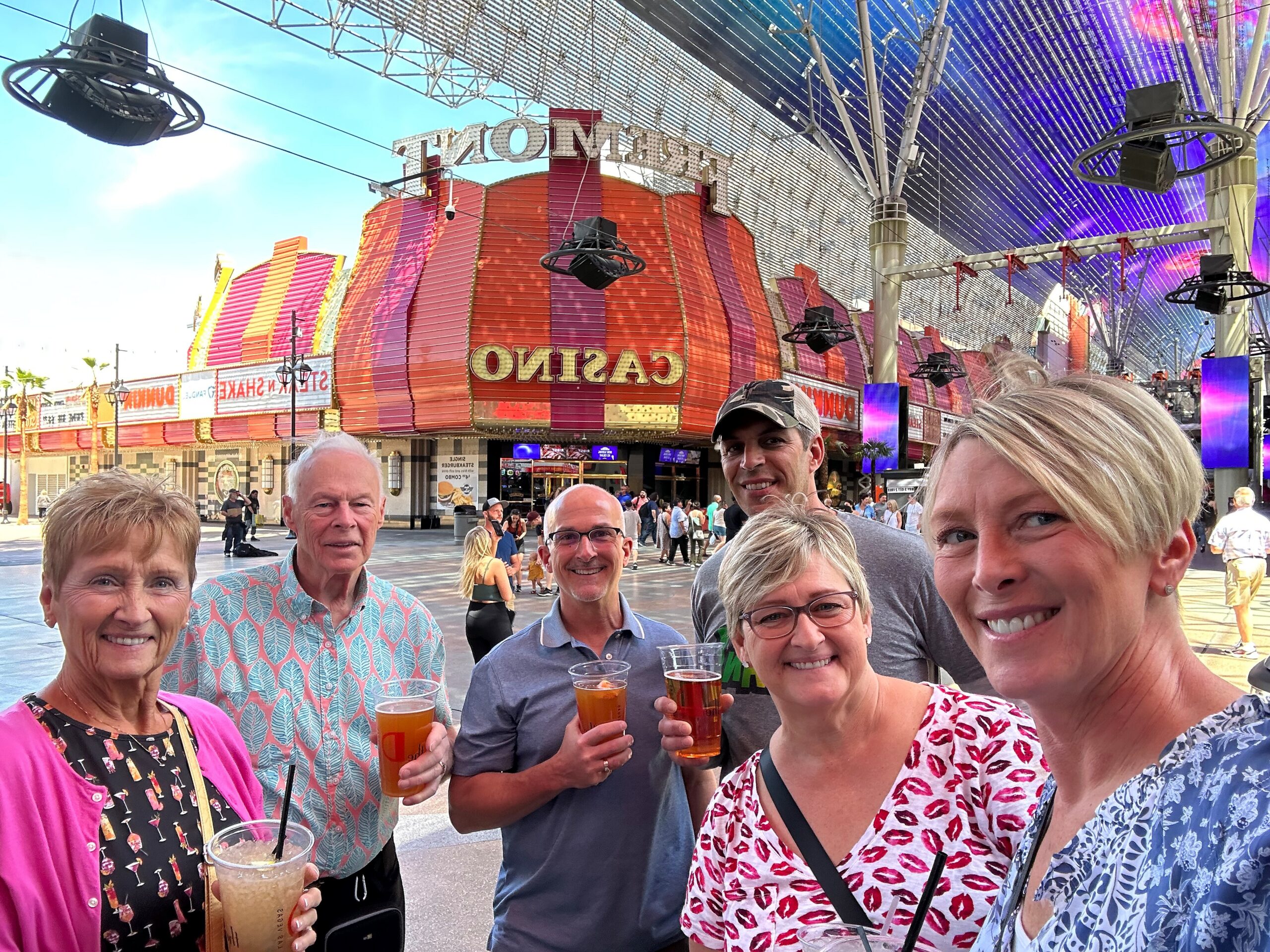 Group of adults smiling for a selfie with a colorful casino facade and drinks in hand in front of them.