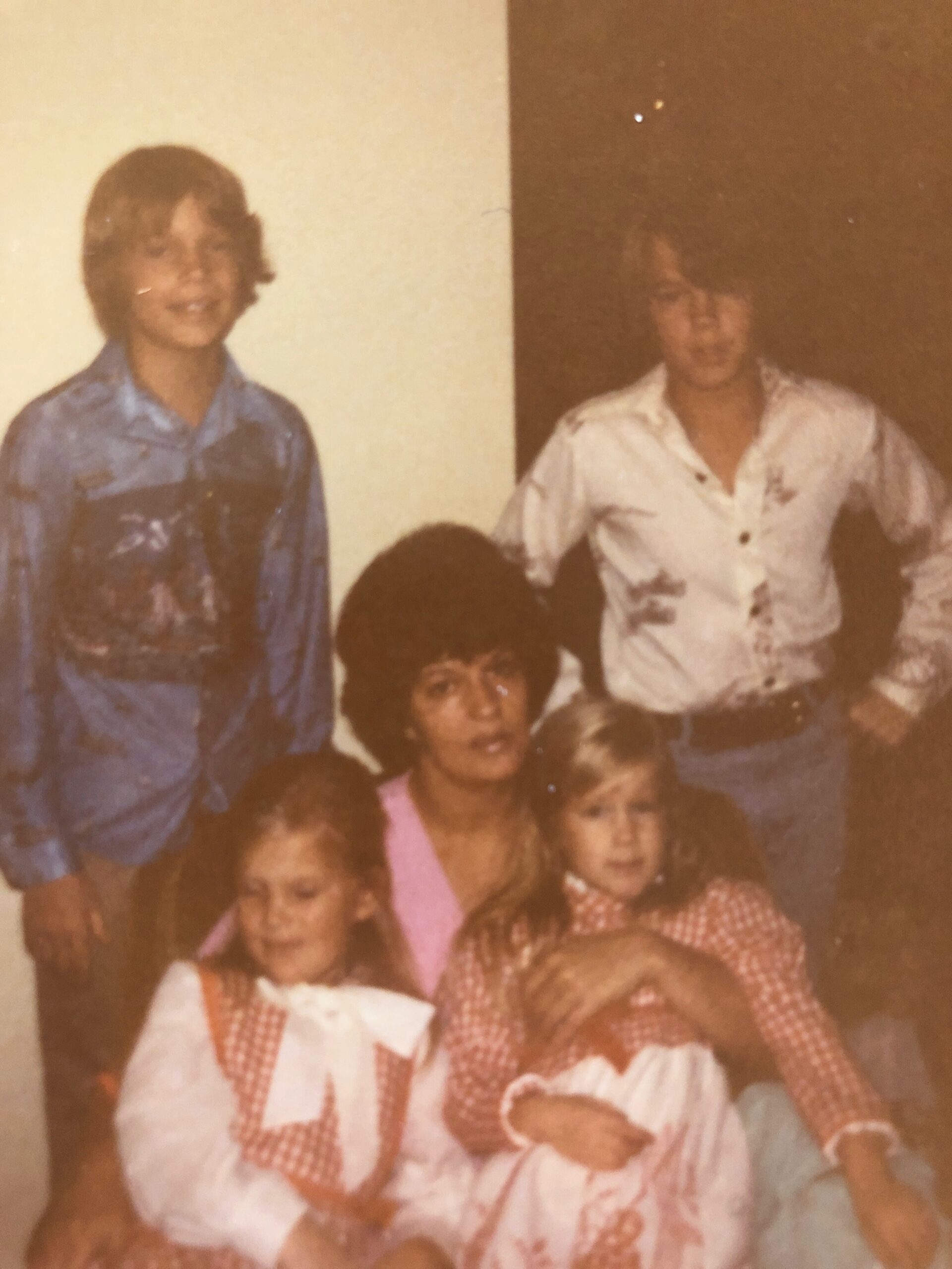 Old family portrait: two adults standing in back, one in a blue shirt and the other in a light patterned shirt, with several children seated in front wearing red-and-white gingham outfits.