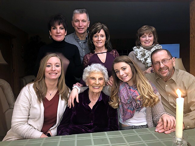 Eight relatives posing around a dining table in a home, smiling at the camera with a lit candle nearby.