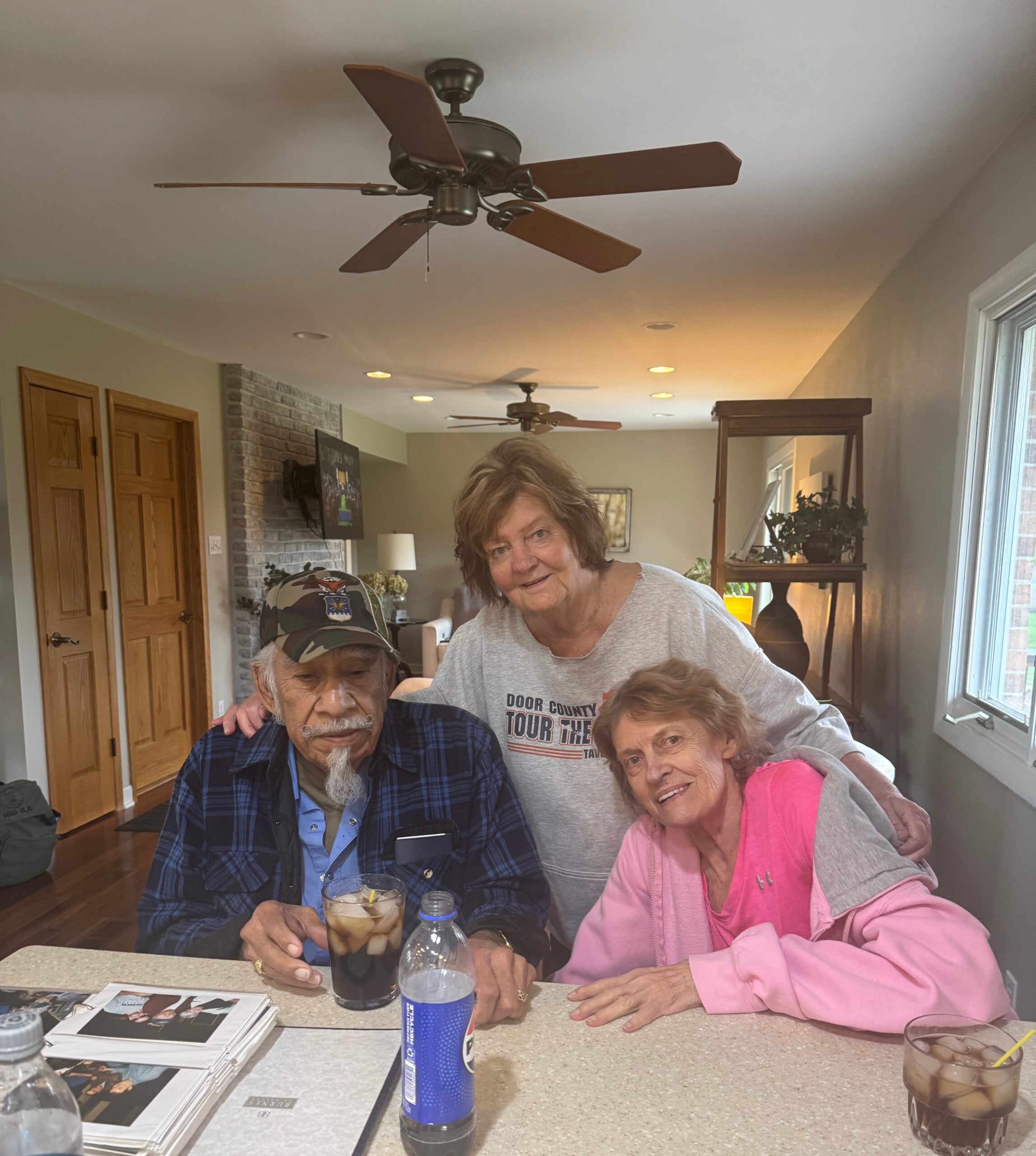 Three older adults sit at a kitchen island with drinks and magazines, posing for a photo in a bright home setting.