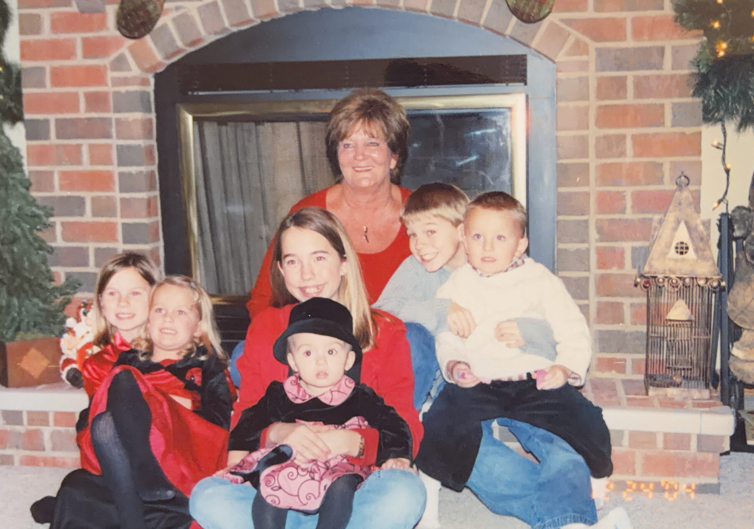 Family group wearing Halloween costumes posing together in front of a brick fireplace, smiling for a holiday photo.