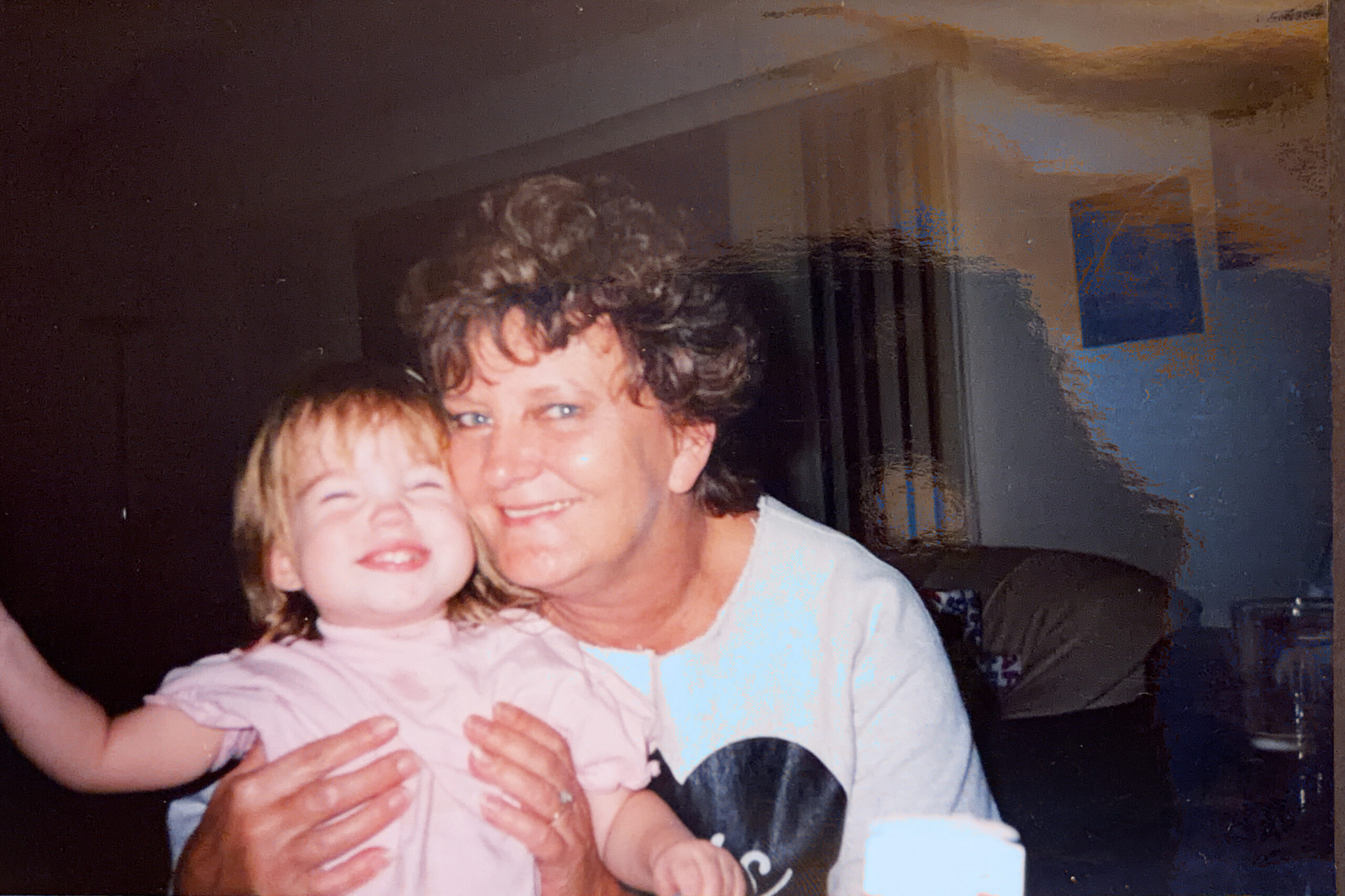 Smiling woman cradling a baby indoors, both looking at the camera.