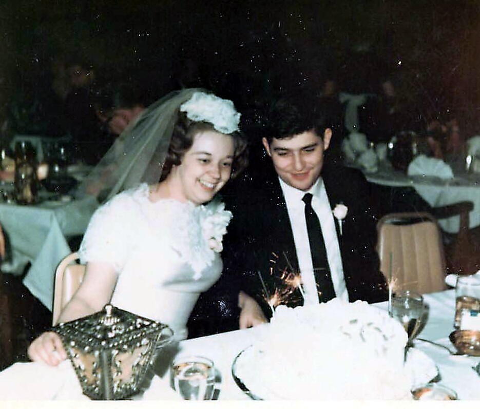 Bride and groom at a wedding reception cutting a cake, smiling as sparklers glow from the cake centerpiece.