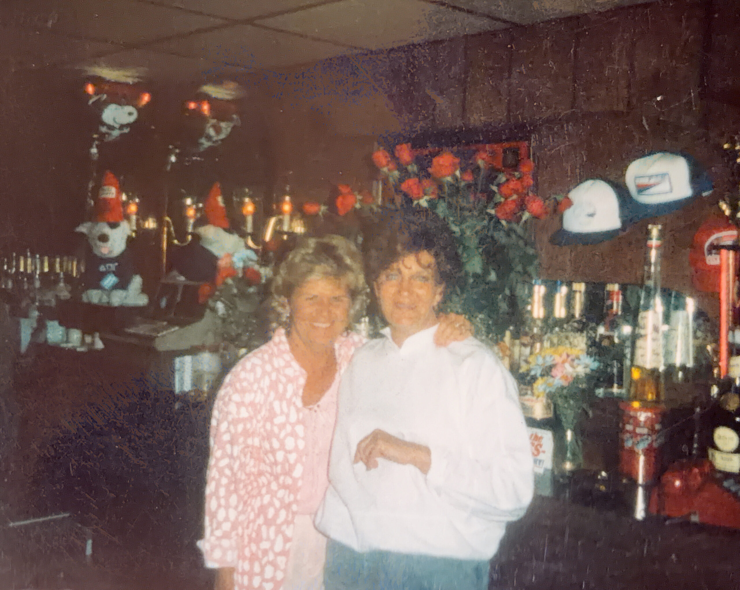 People posing for a photo in a bar or party setting, with drinks on the counter and festive decorations in the background.