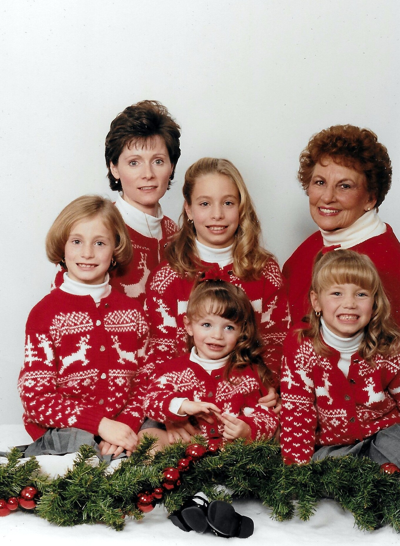 A group of six people wearing red and white Nordic sweaters posing for a holiday family portrait, with a garland in the foreground.