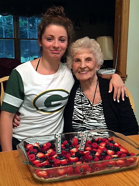 Two women, a younger and an older, smile while sitting at a table with a berry dessert in a glass pan in front of them.