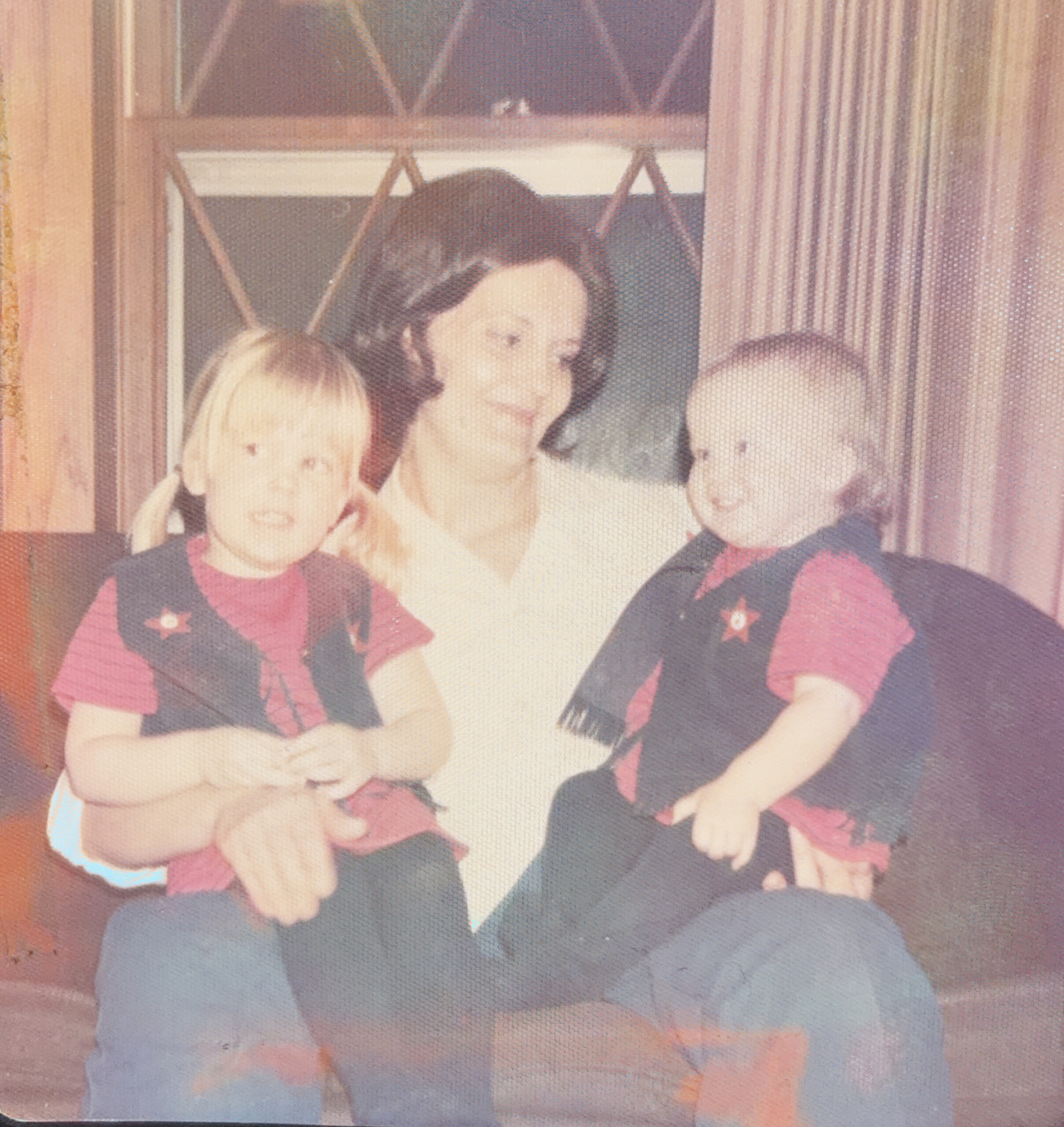 Three people—a woman in the center flanked by two children—pose together by a window, wearing matching argyle sweaters.