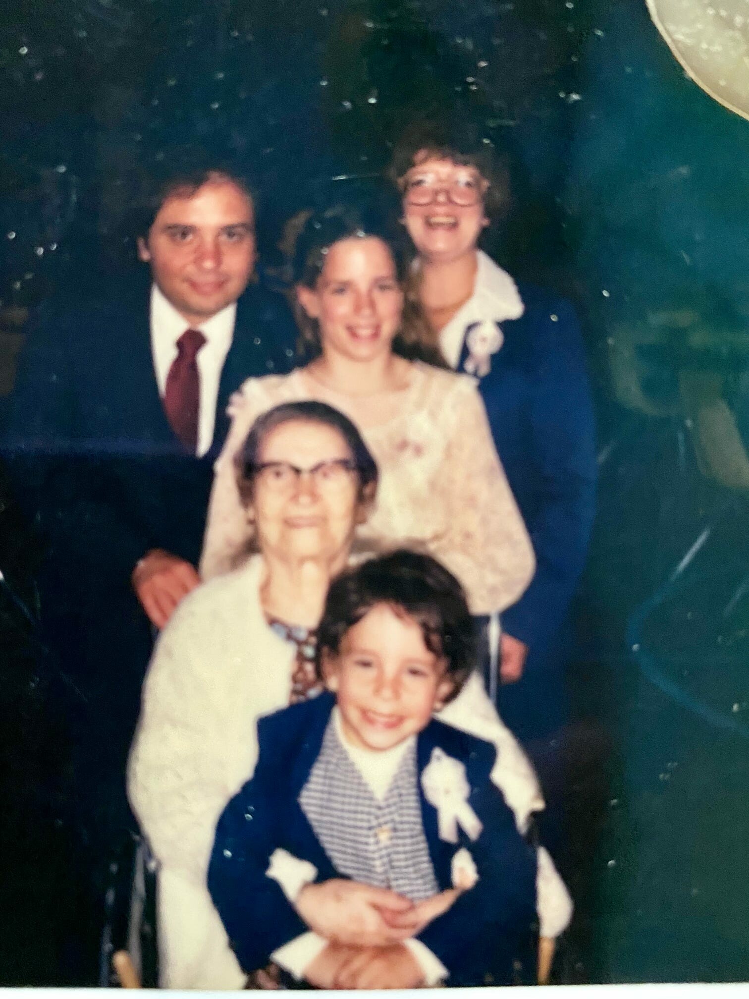 Group of people posing for a family photo at a formal event, with a man in a suit and a woman with glasses in the back row and children in front.