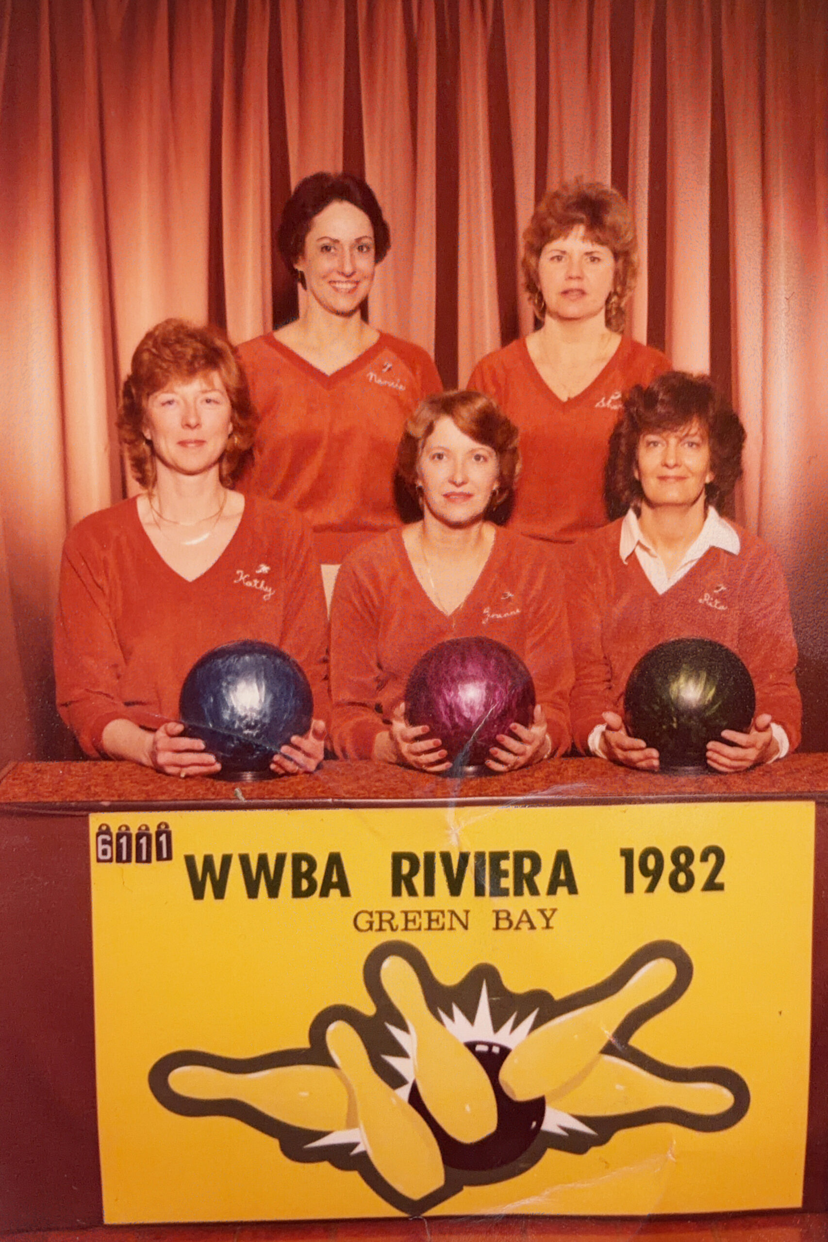 Five women in matching red shirts pose with colored bowling balls in front of a yellow WWBA Riviera 1982 sign, Green Bay, a vintage bowling team photo.