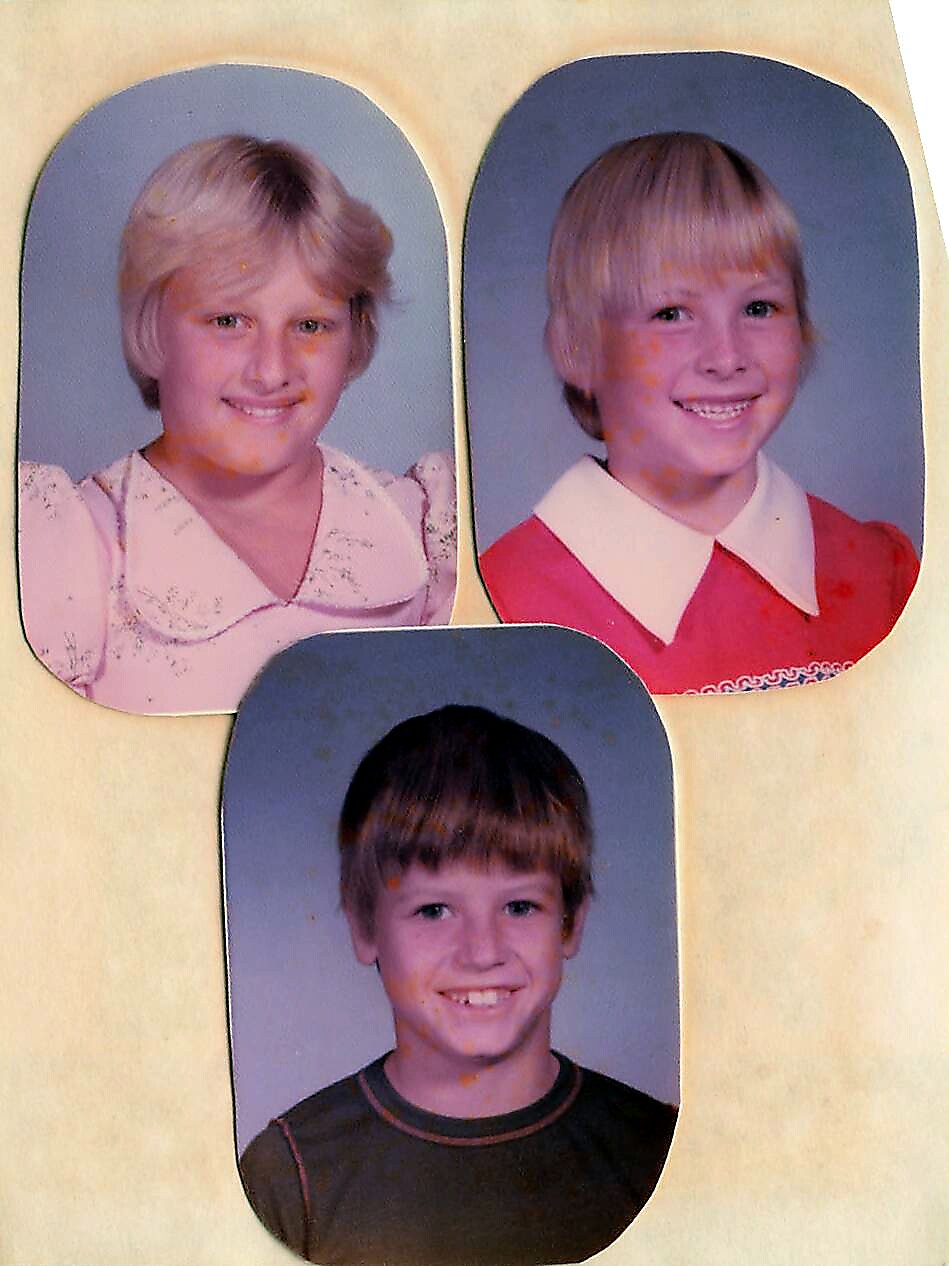 Three school portrait photos arranged on a cream page: top left a blonde girl in a light pink blouse, top right a smiling blonde girl in a red dress with white collar, bottom center a smiling boy with brown hair in a dark shirt.