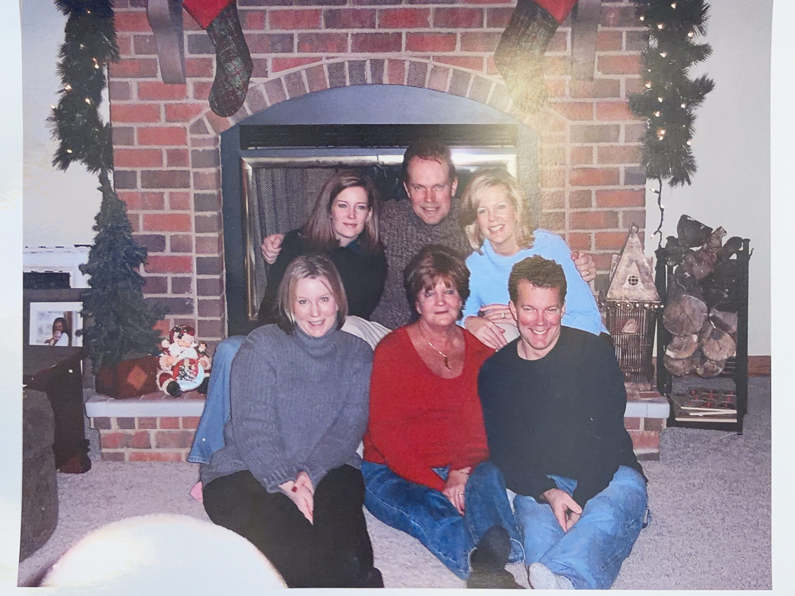 Family group posing in a living room in front of a brick fireplace decorated for Christmas.