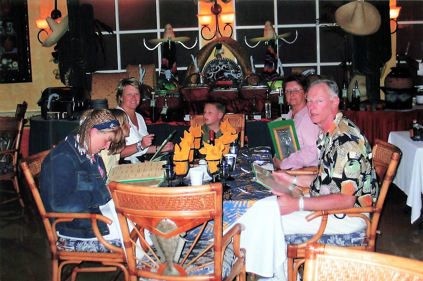 Group of six people seated around a round table in a tropical-themed restaurant, sharing a meal and looking at the camera.