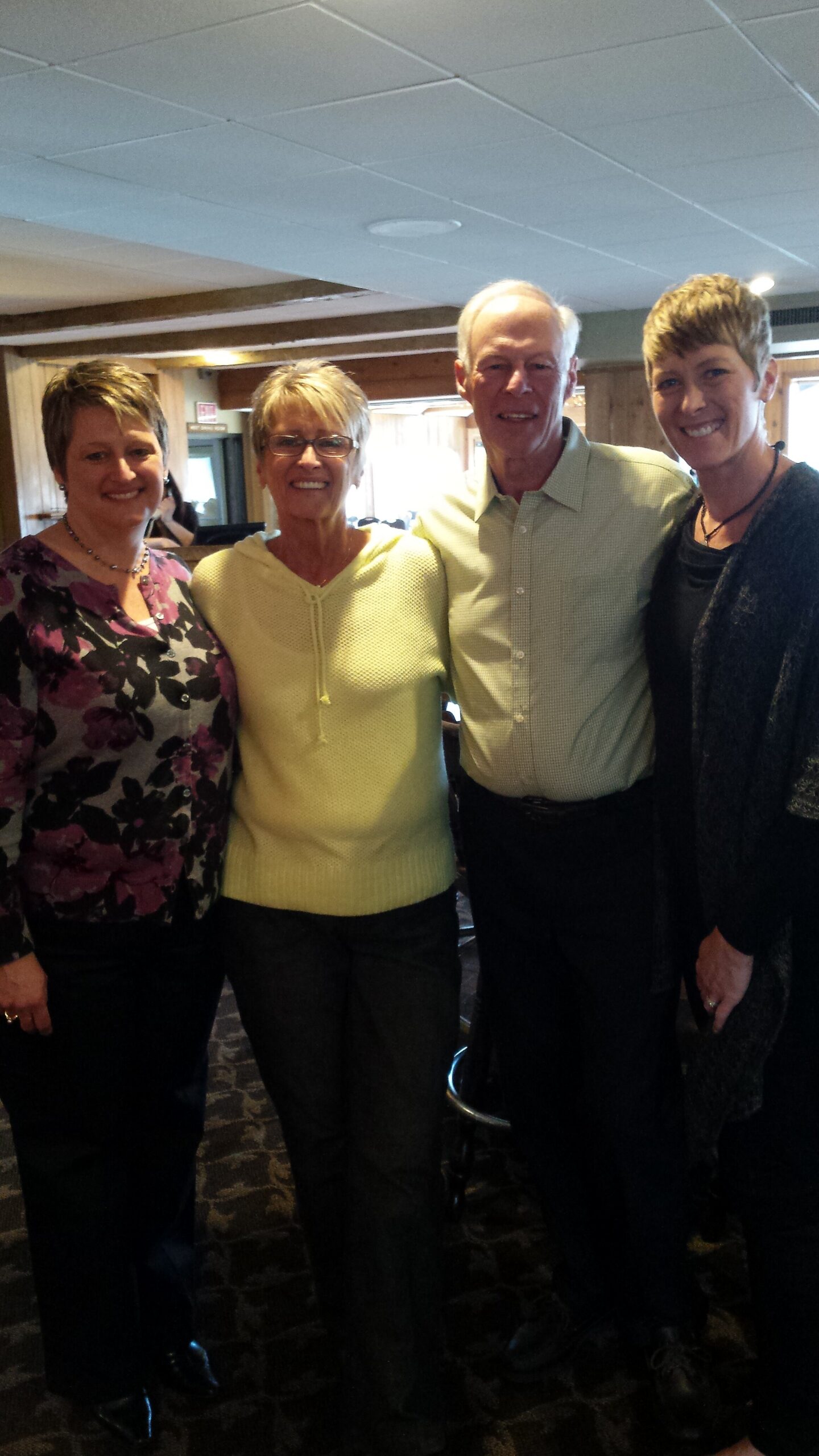 Four adults standing together indoors, smiling at the camera.