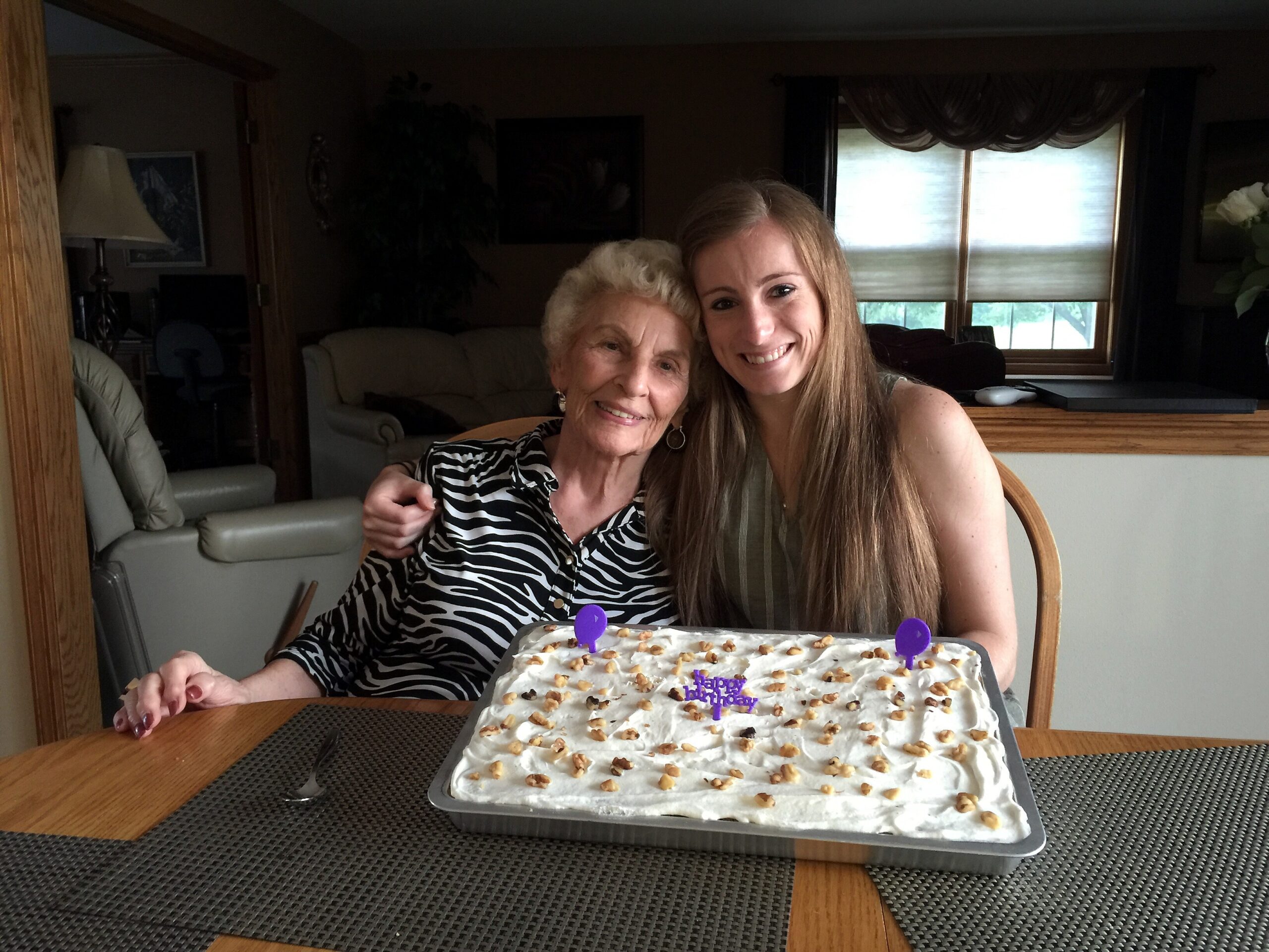Two women smiling at a birthday cake on a table, celebrating indoors.