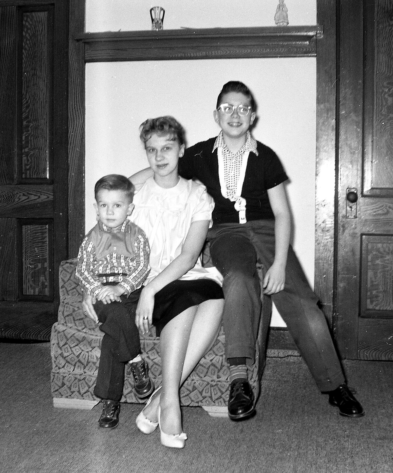Three children sit on a patterned armchair in a doorway, posing for a family photo.