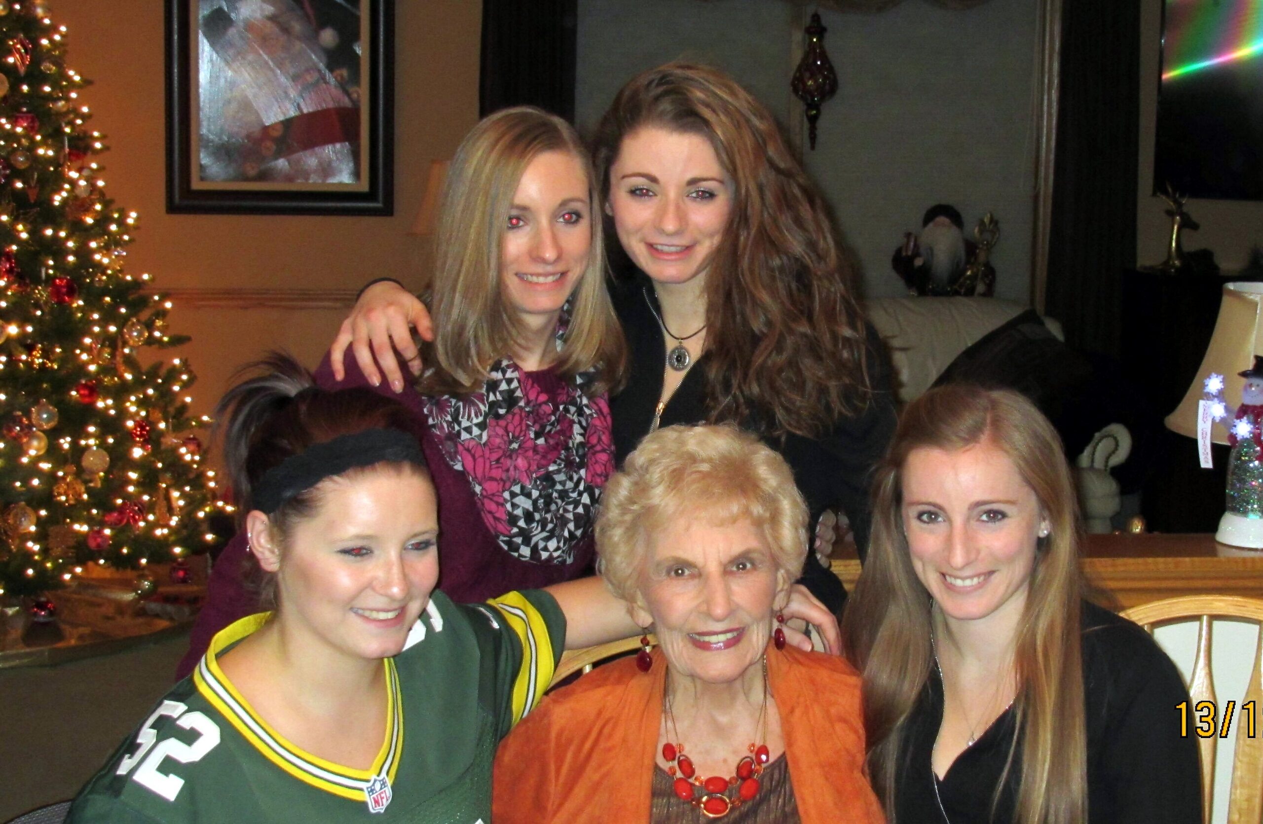 Group of smiling women posing together for a holiday photo beside a decorated Christmas tree indoors.