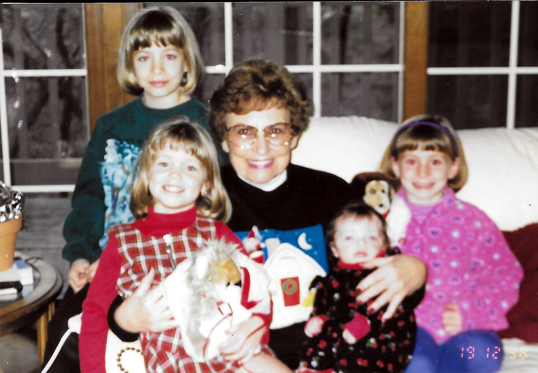 Grandmother with three young girls posing indoors with Christmas gifts.