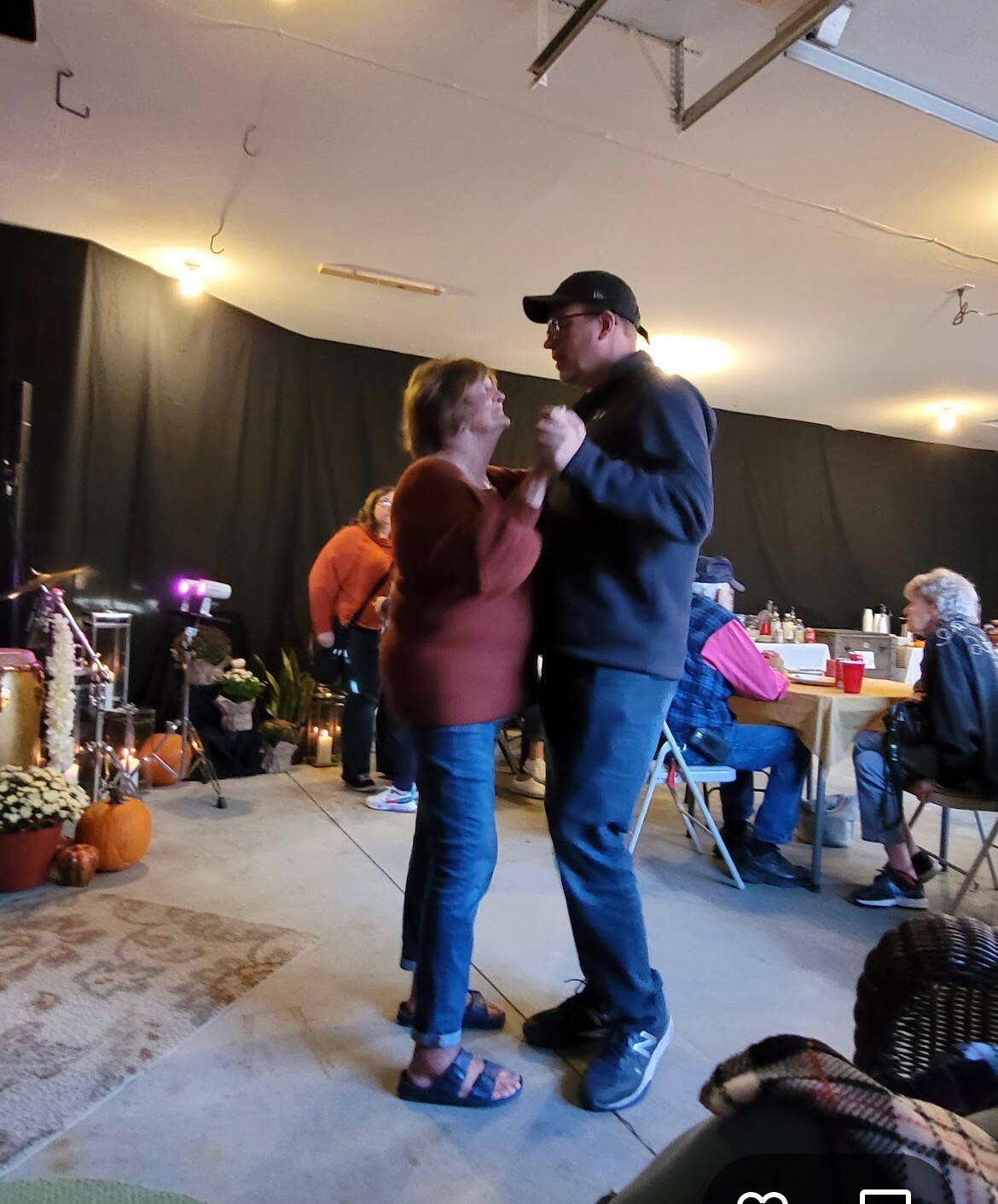 Couple dancing closely in a casual indoor gathering with pumpkins and flowers nearby.