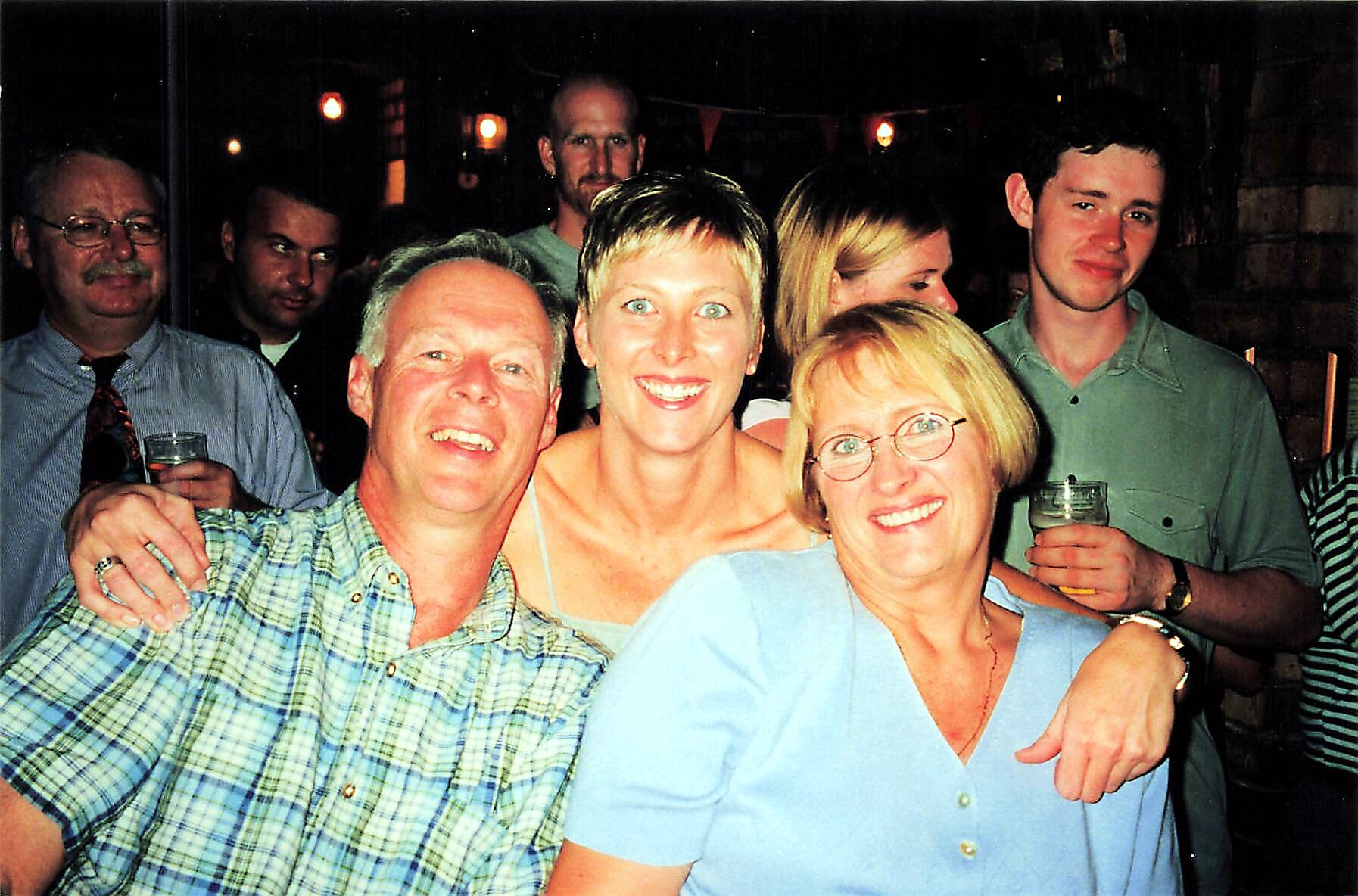 Group of seven adults at a party, smiling for the camera with drinks in hand.
